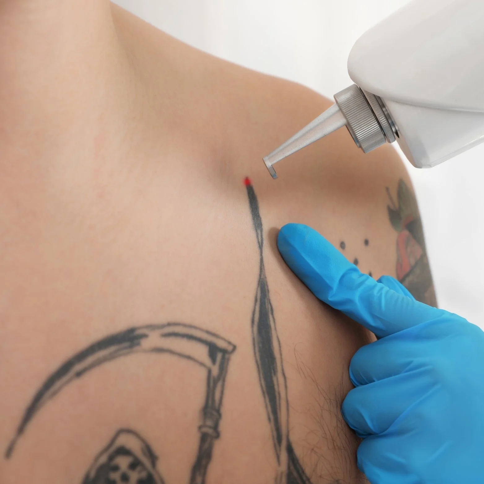 A person getting a tattoo on their upper shoulder with a tattoo machine, wearing a blue glove.