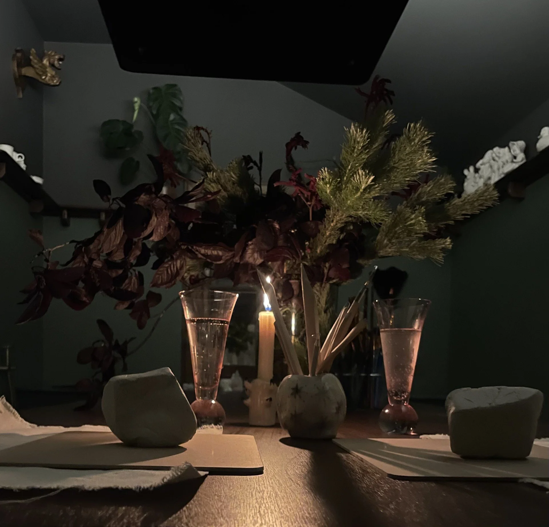 A dark dining table set with two glasses of champagne, a candle, and a floral arrangement in a small jug, with decorative stones and a candle in the background.