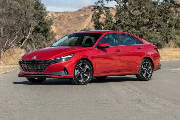 Red Hyundai sedan parked on a paved road with trees and hills in the background.
