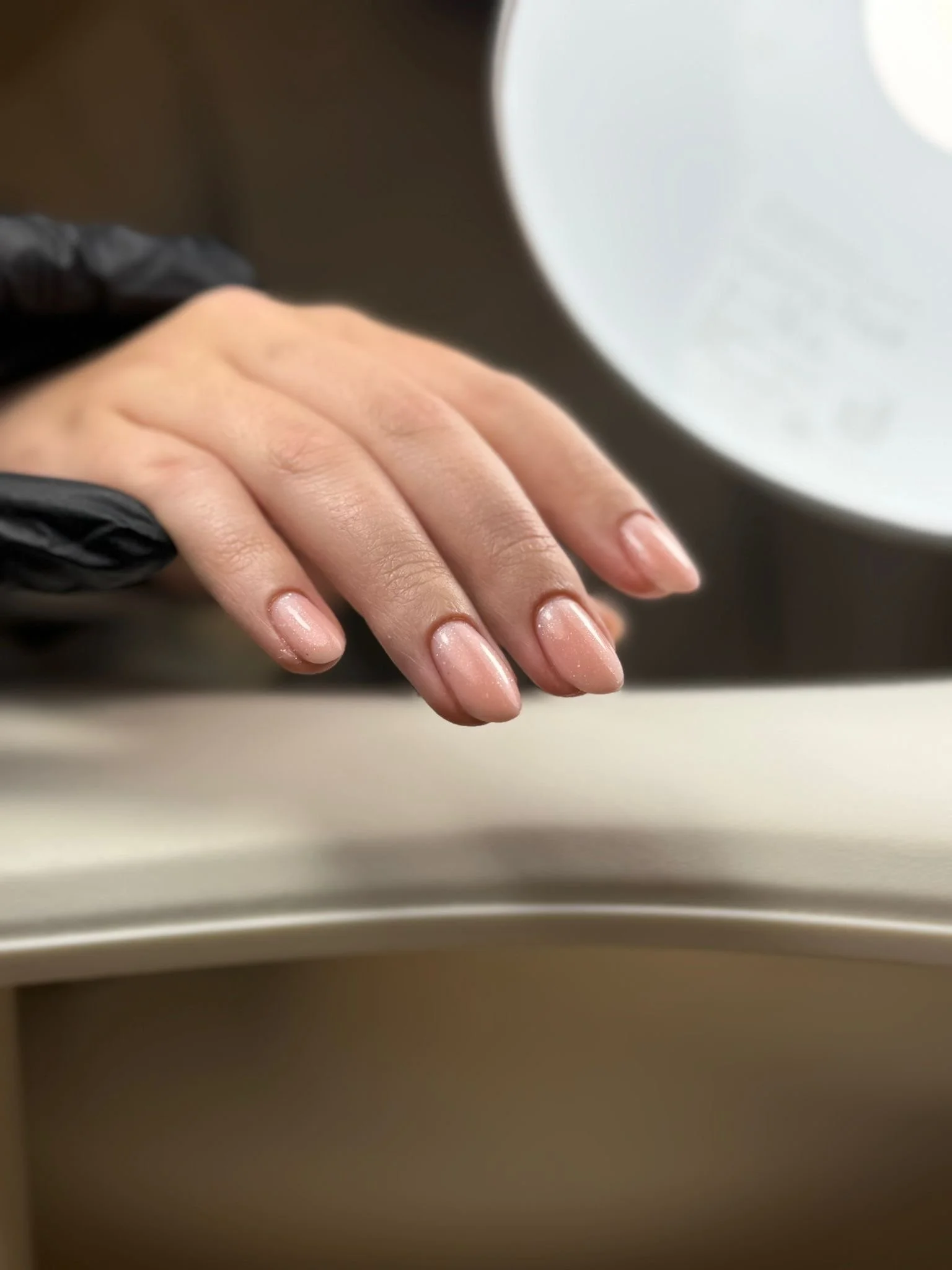 Hand met nette, gepolijste nagels met een lichte ondertoon, rustend op een wit oppervlak.