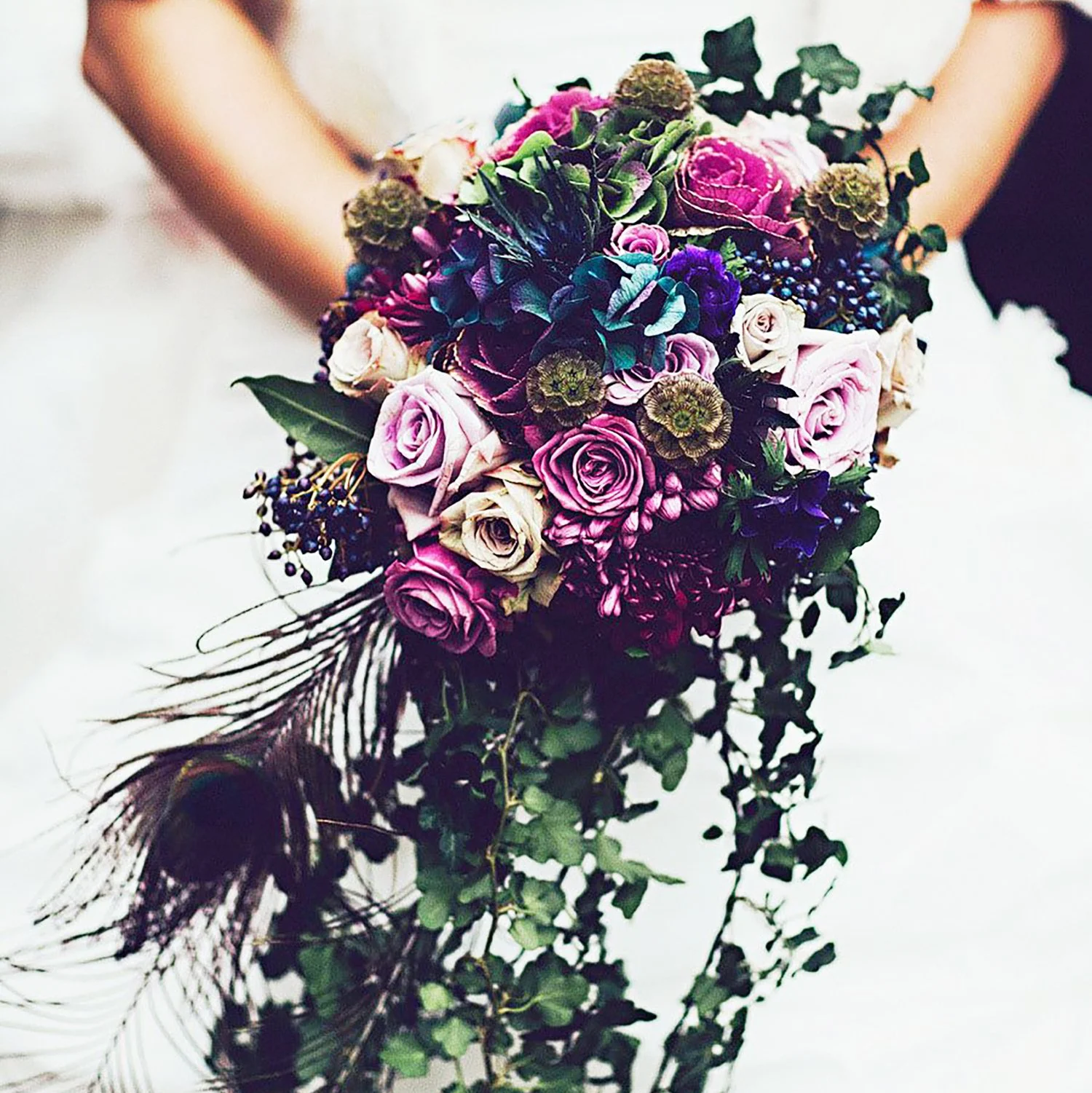 A person's hands holding a vibrant bouquet of assorted flowers including roses, hydrangeas, and greenery, reflecting on a surface.