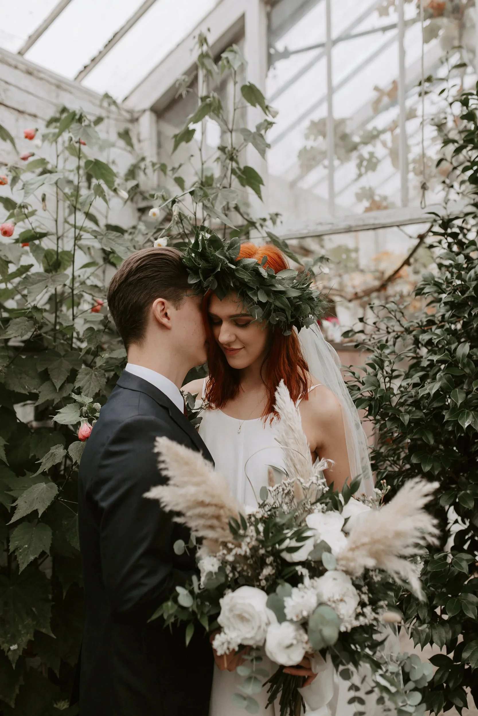 A bride and groom embracing during their wedding ceremony in a greenhouse surrounded by greenery and flowers.