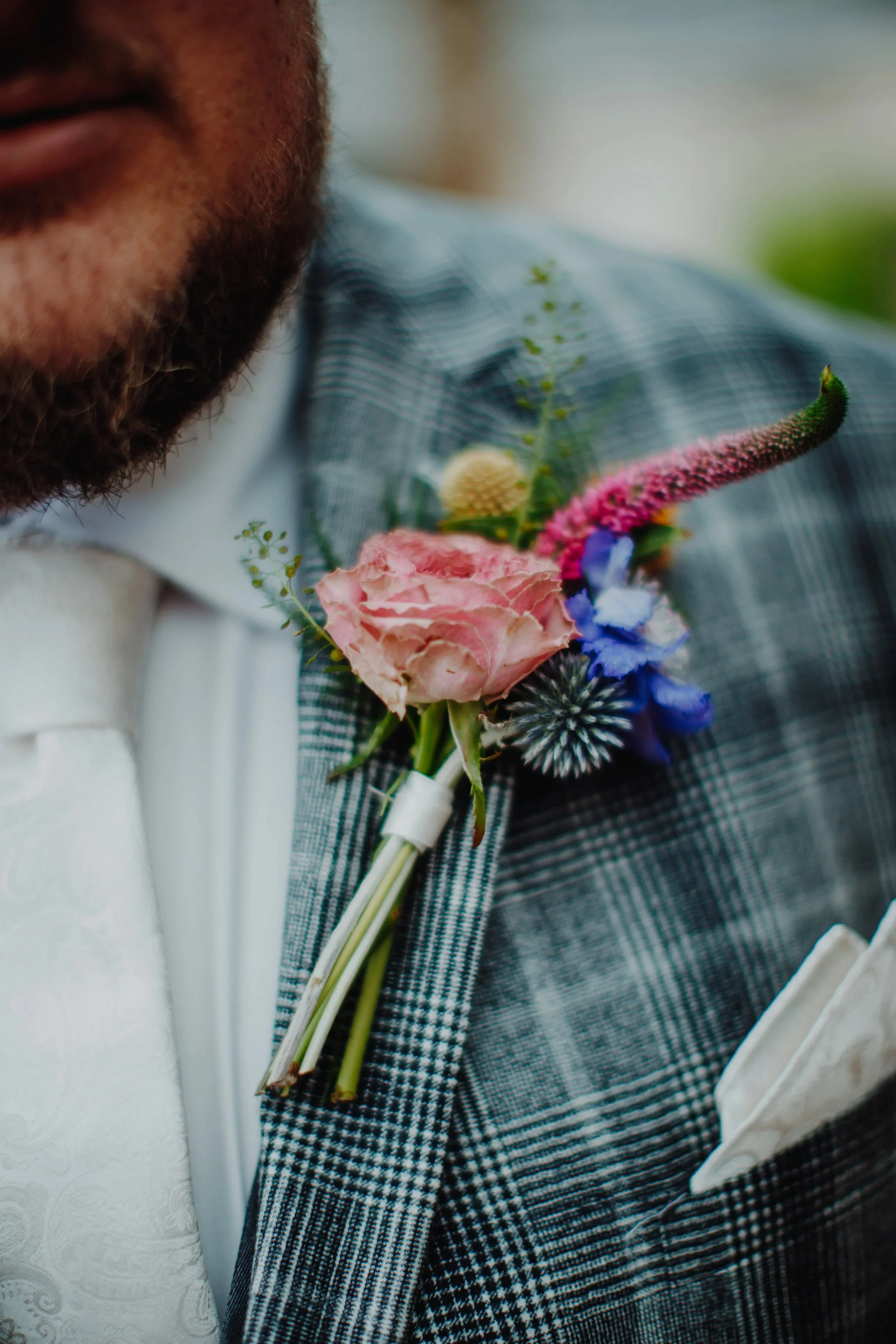 Close-up of a man wearing a black and white checkered suit with a boutonniere made of pink, purple, and yellow flowers pinned to his lapel.