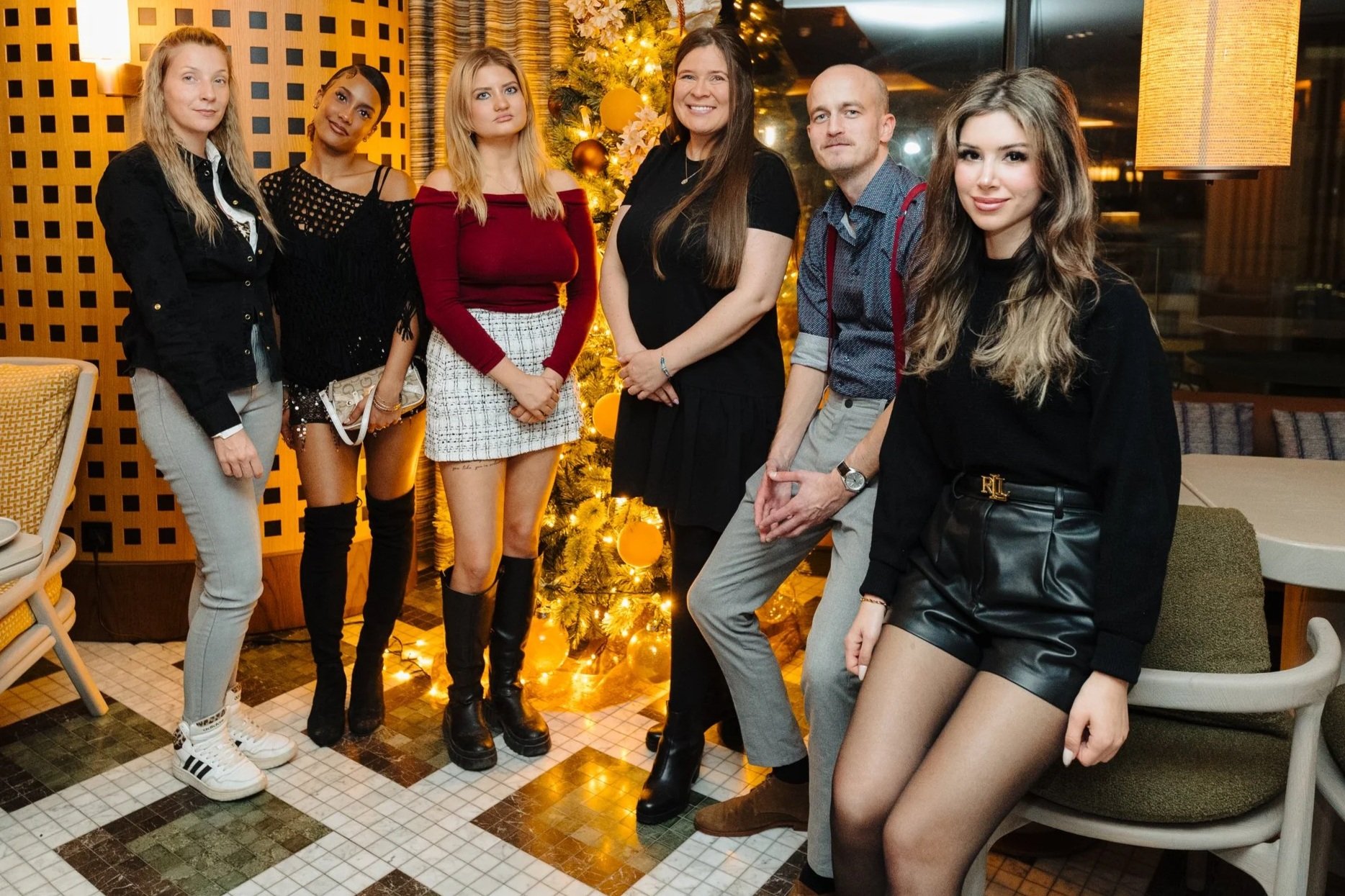 Group of six people standing in front of a decorated Christmas tree in a restaurant.
