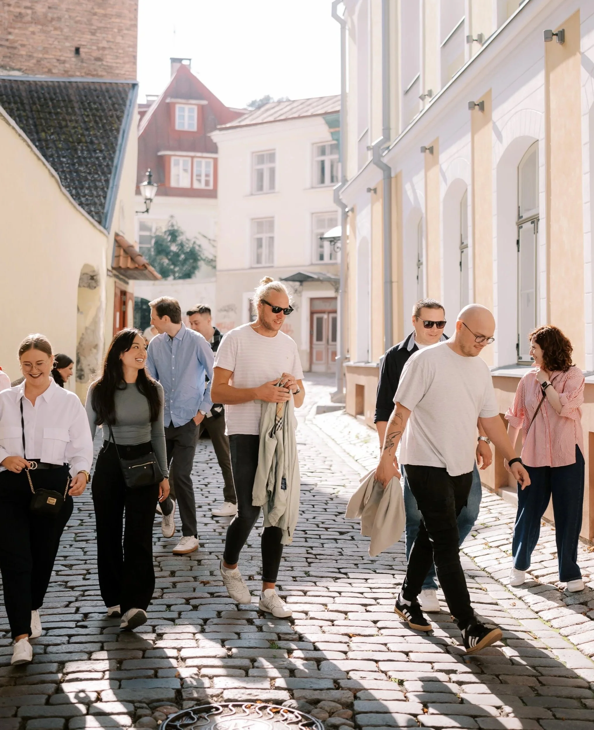 Group of people walking on cobblestone street in a sunny urban area with colorful buildings.