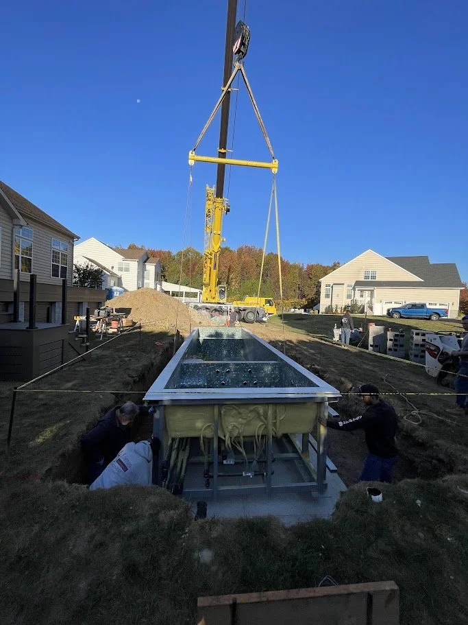 Construction workers installing a large above-ground water tank in a residential backyard, with a crane lifting the tank into place.