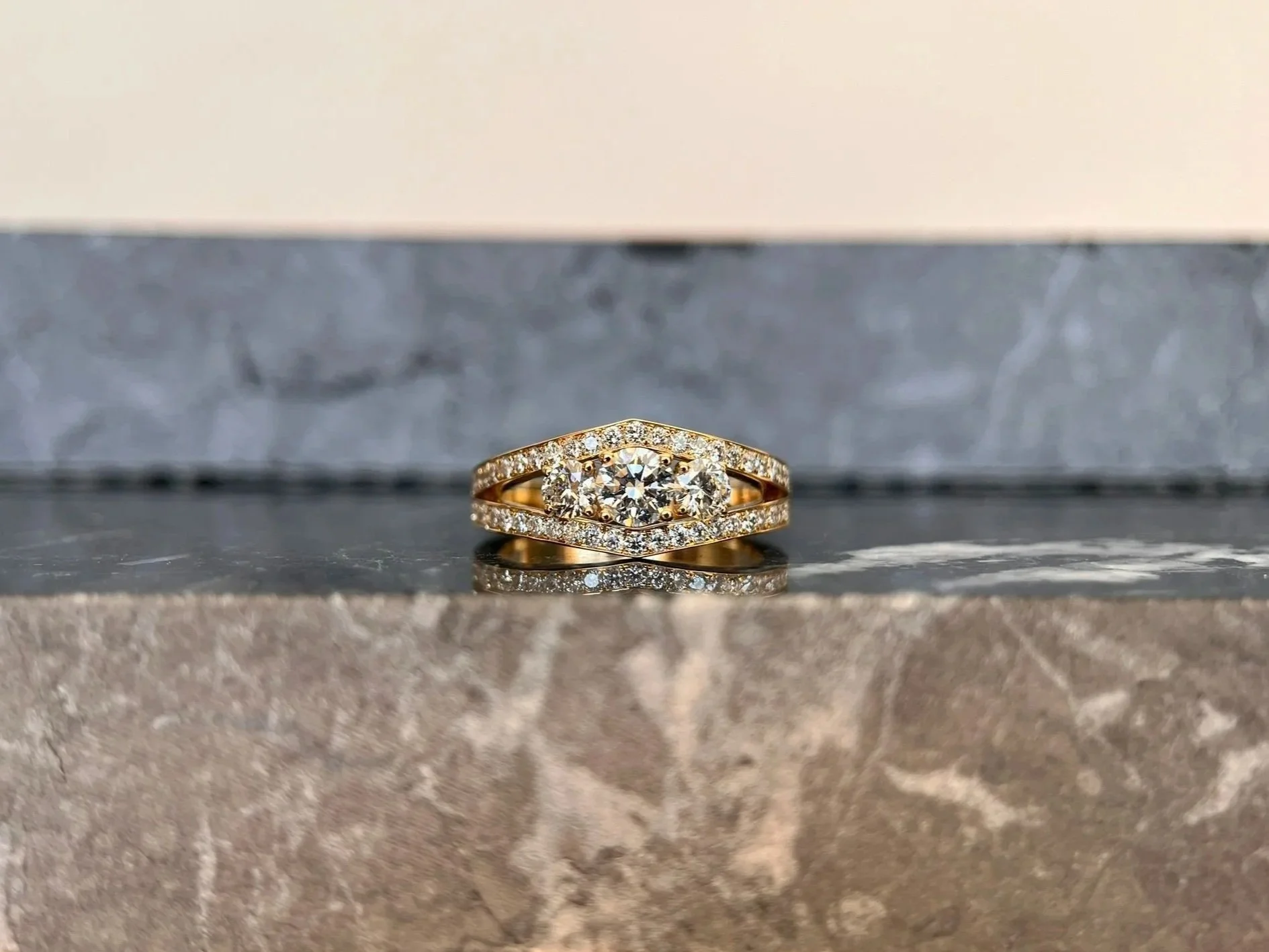 Bague en or avec un grand diamant central entouré de petits diamants, posée sur une surface en pierre naturelle.