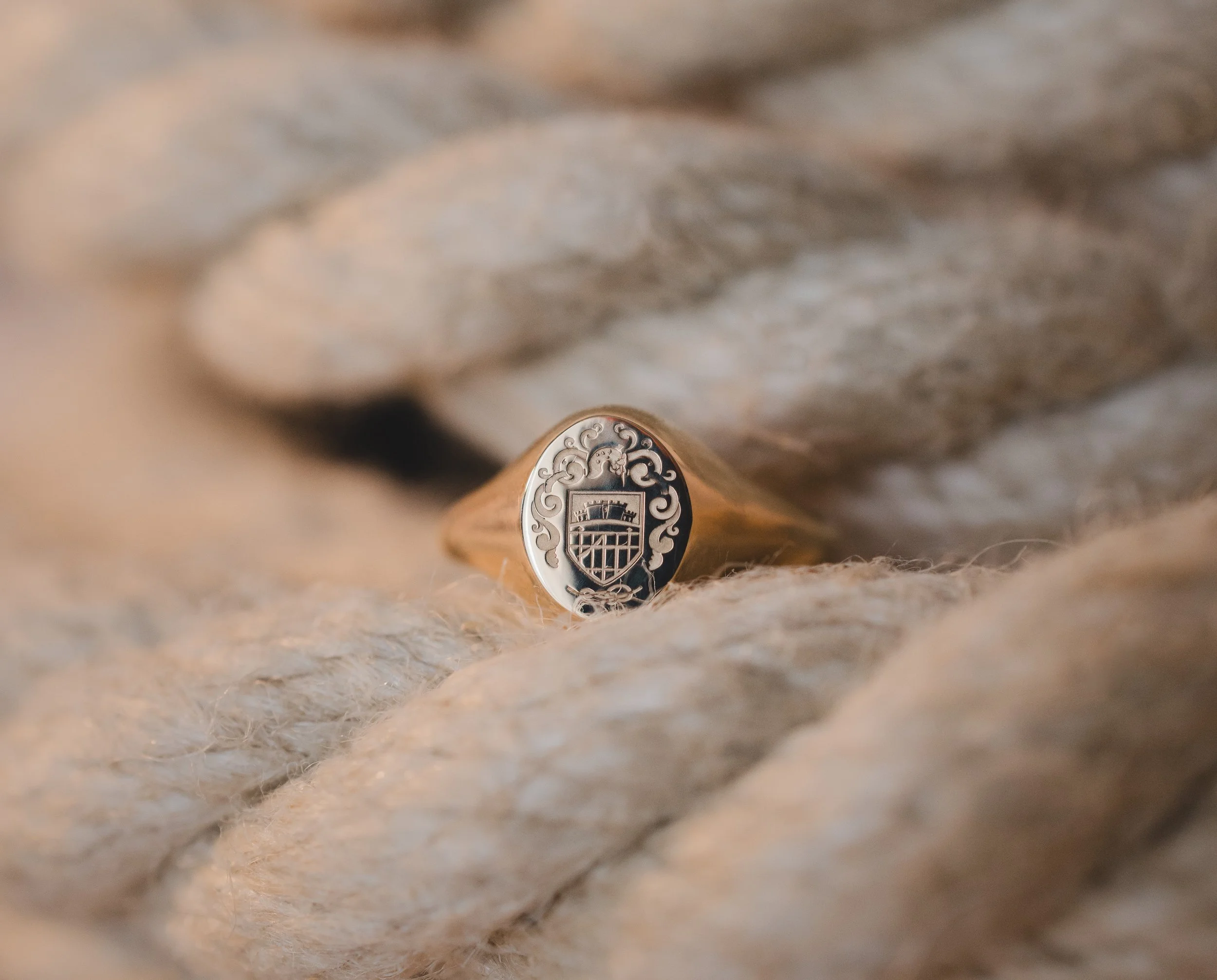 Une bague en or reposant sur une corde épaisse, avec un motif complexe et un symbole gravé sur le dessus.