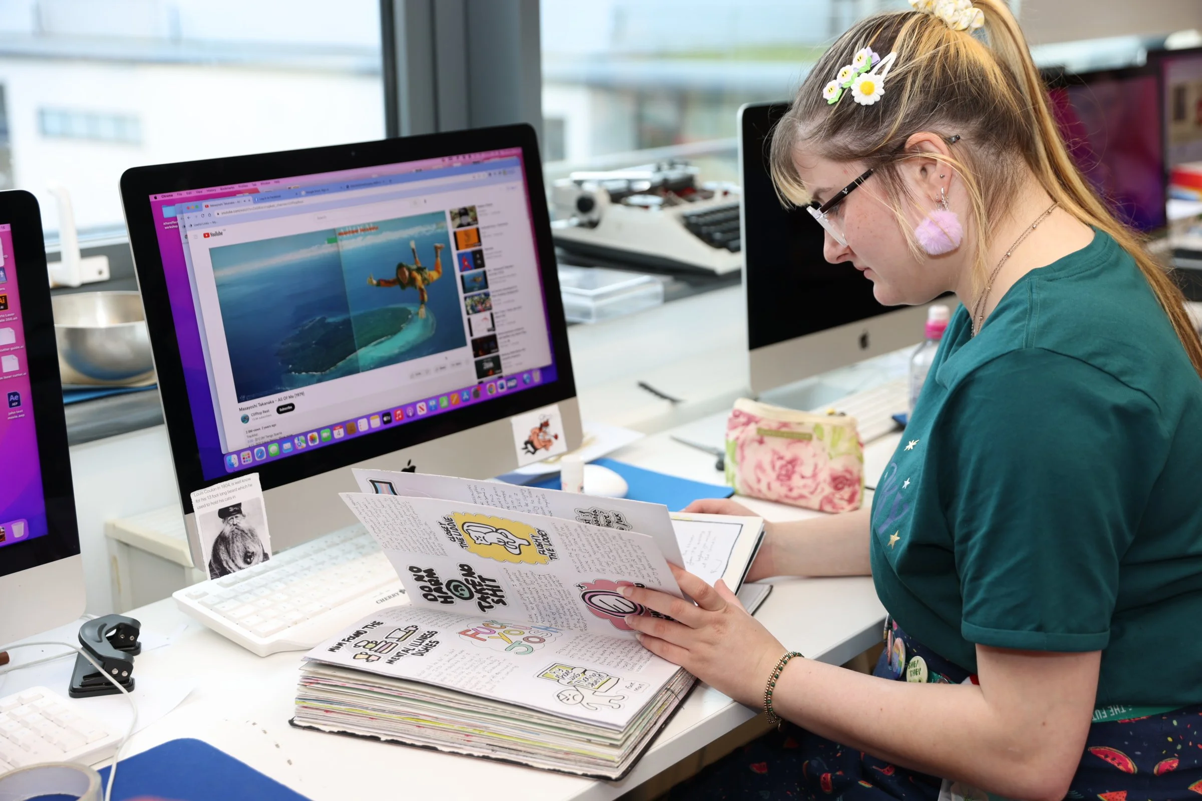 A student working on a Mac and reflecting on their work in a sketch book