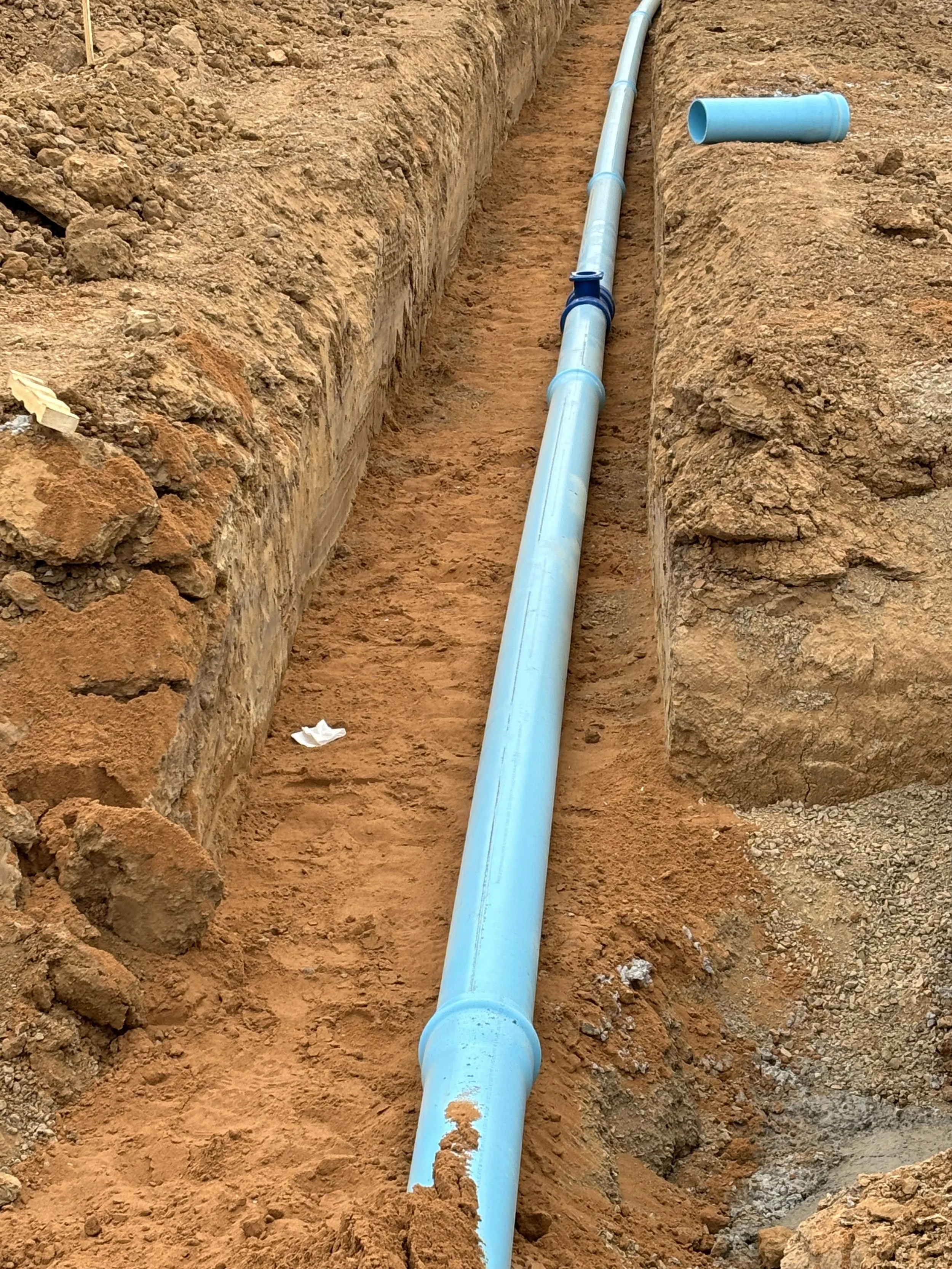 Blue PVC pipe installed in a narrow trench in the ground for underground plumbing or sewer line.