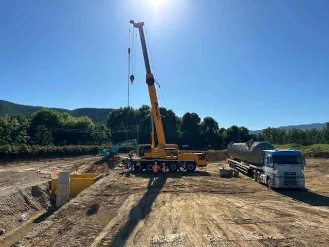 Construction site with a large yellow crane lifting materials, a white semi-truck, and excavators