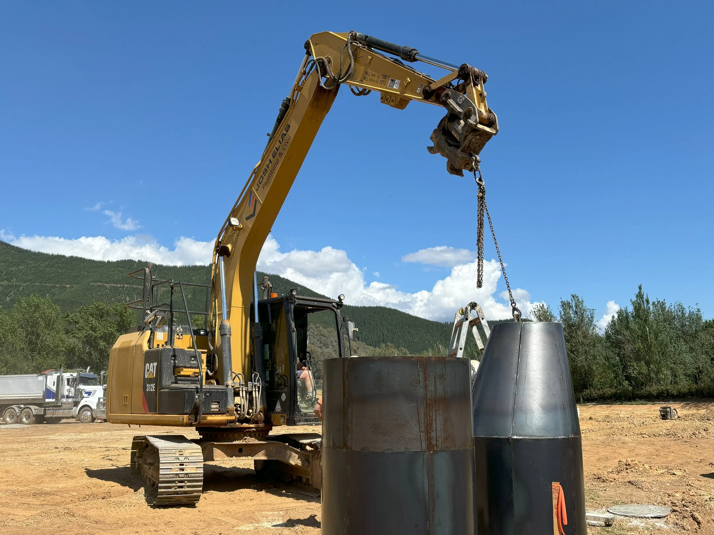 A yellow excavator lifting a large pipe at a construction site