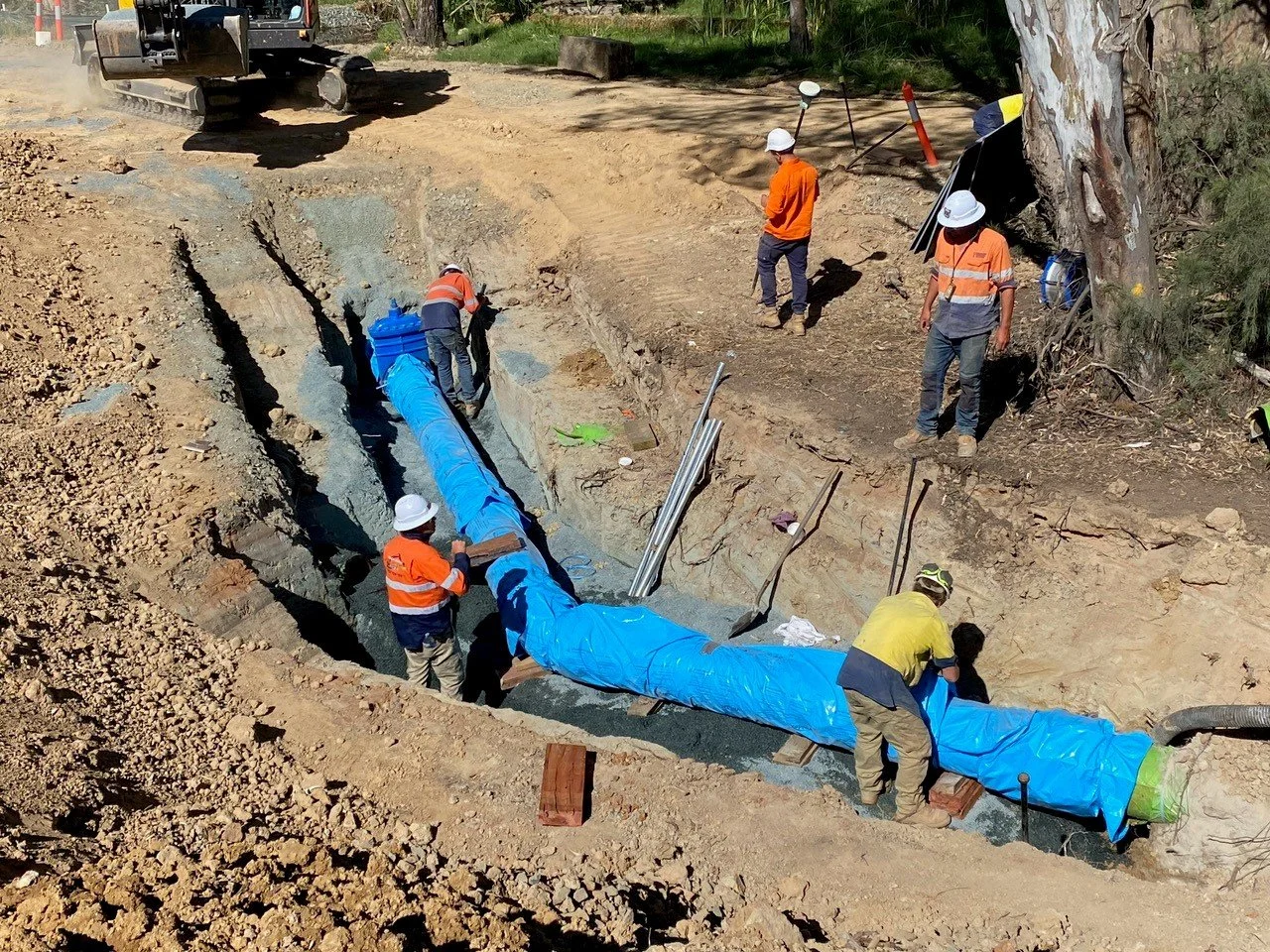 JEPC TEAM installing a large blue pipe into the ground at a construction site, with machinery and tools visible.