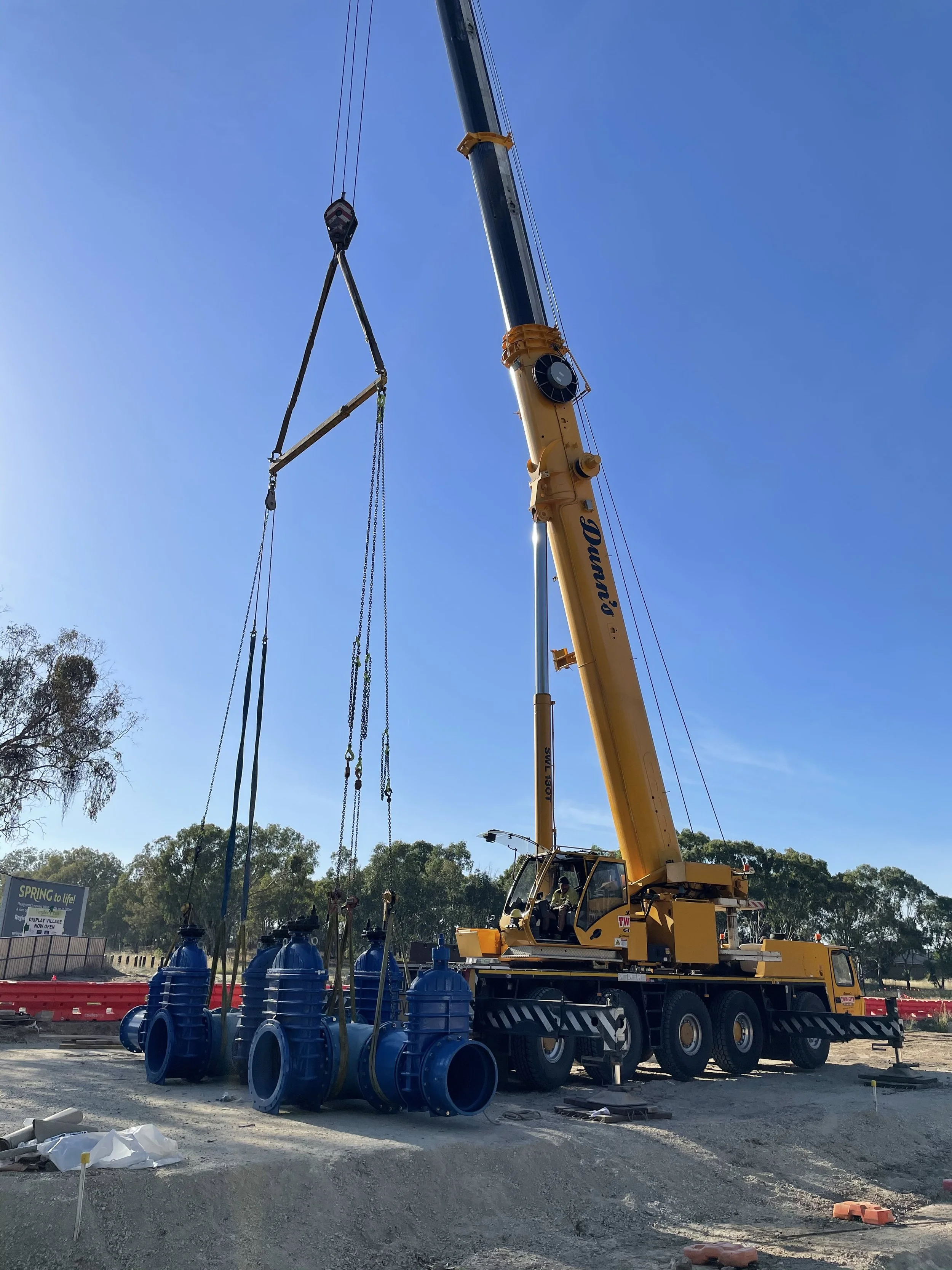 Construction site with a yellow crane lifting large blue valves under a clear blue sky.