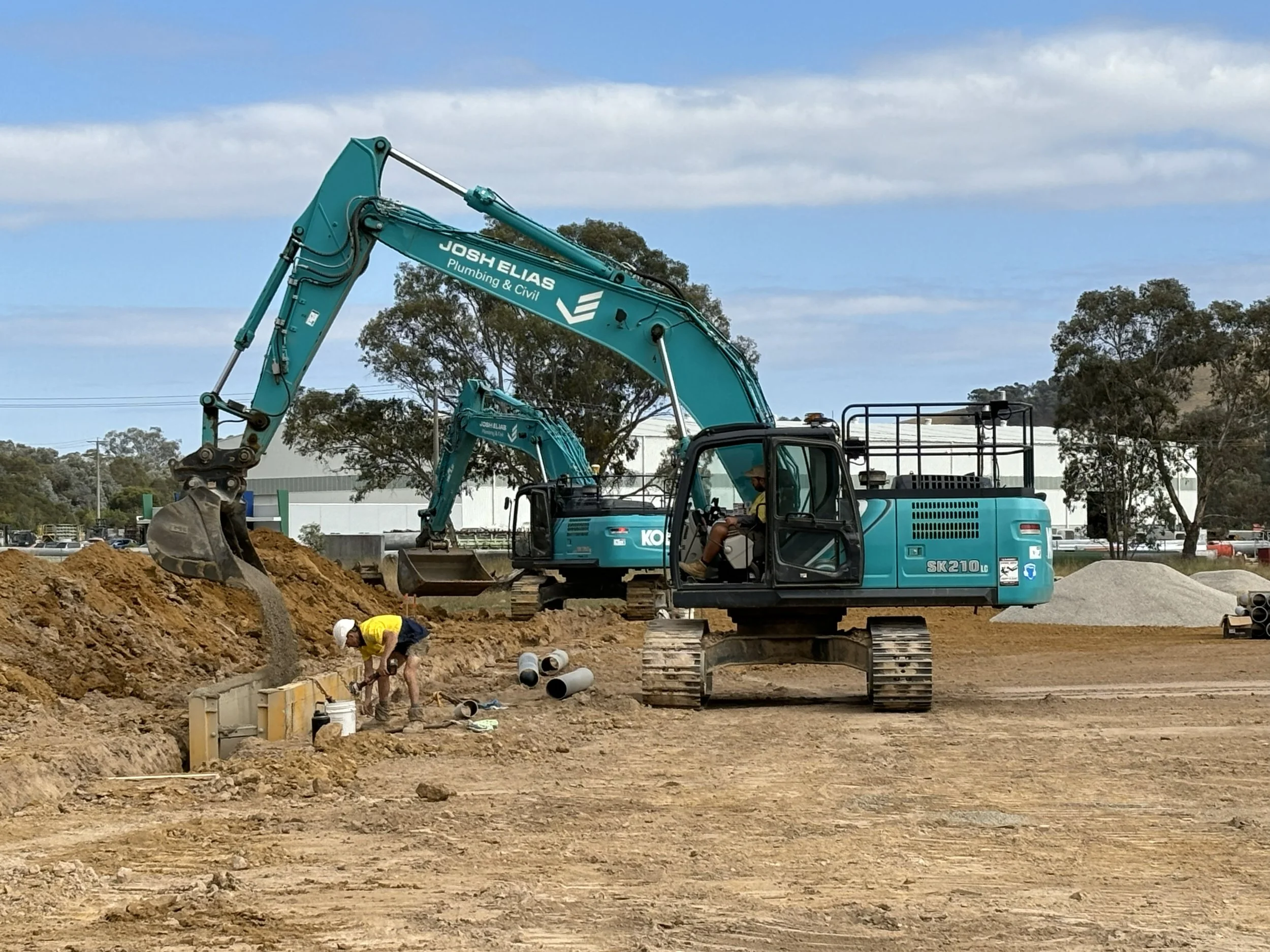 Construction site with two JEPC excavators and a worker installing underground pipes