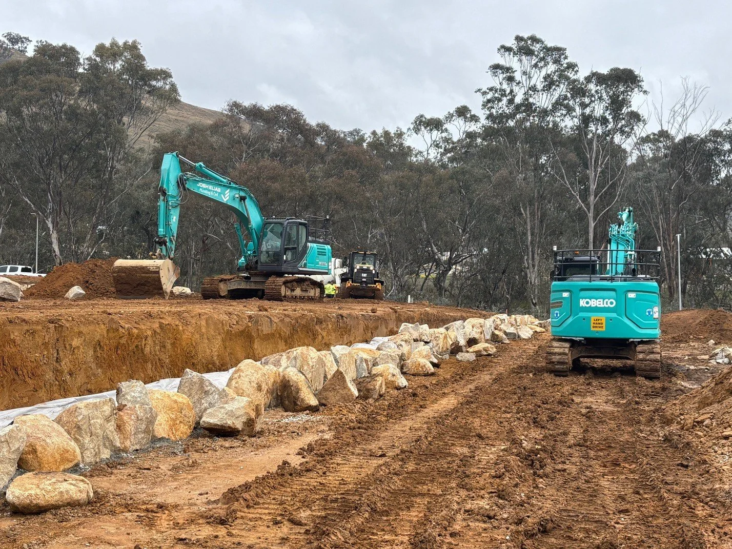 Construction site with two JEPC excavators and a bulldozer working on a dirt road, with rocks lined along the edge a