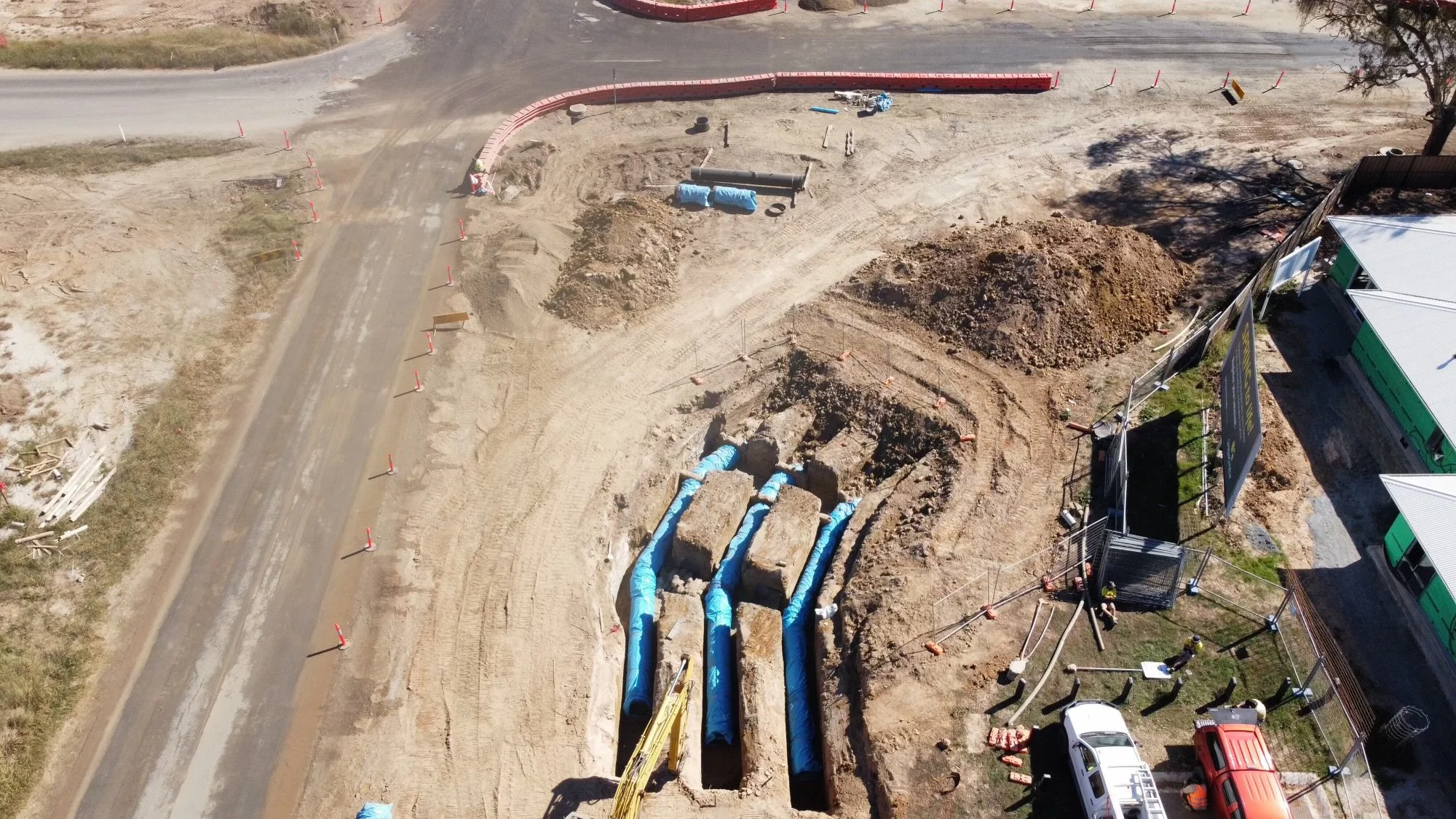 Construction site with excavation and pipelines, surrounded by safety barriers and equipment.