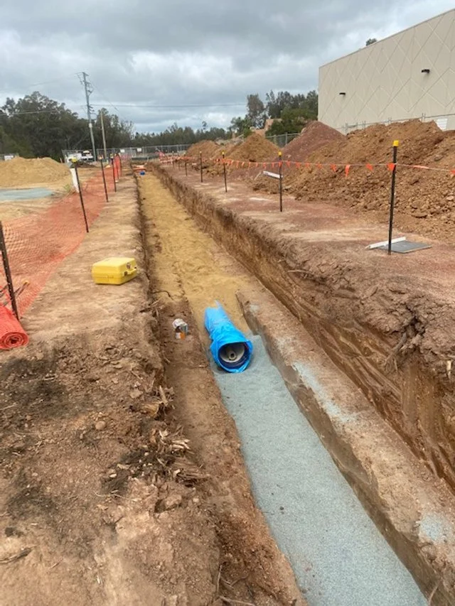 Construction site with a long trench for laying pipes, fencing, and equipment