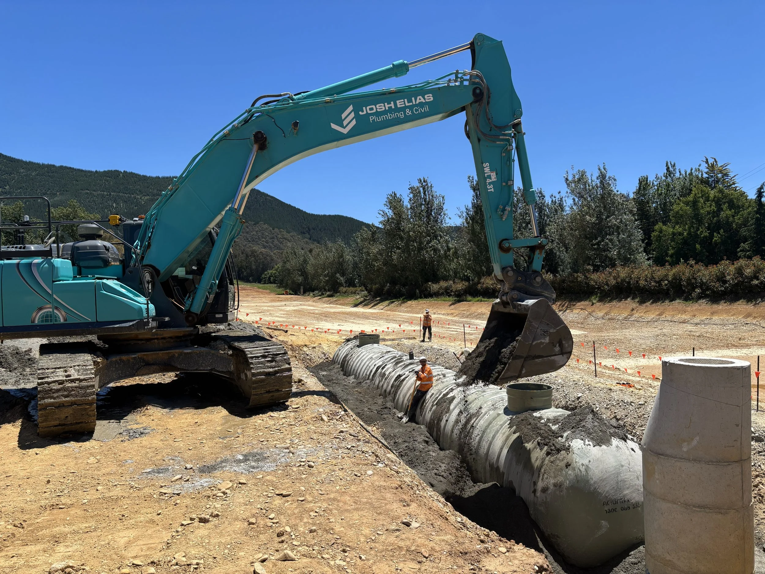 Construction site with a large JEPC excavator working on a pipeline, with two workers in safety gear nearby