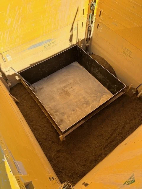 rectangular metal frame on a dirt floor, surrounded by yellow insulation panels and a black mat.