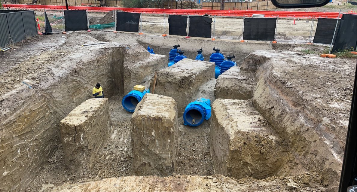 Construction site with large excavated trench and multiple blue pipes being installed underground