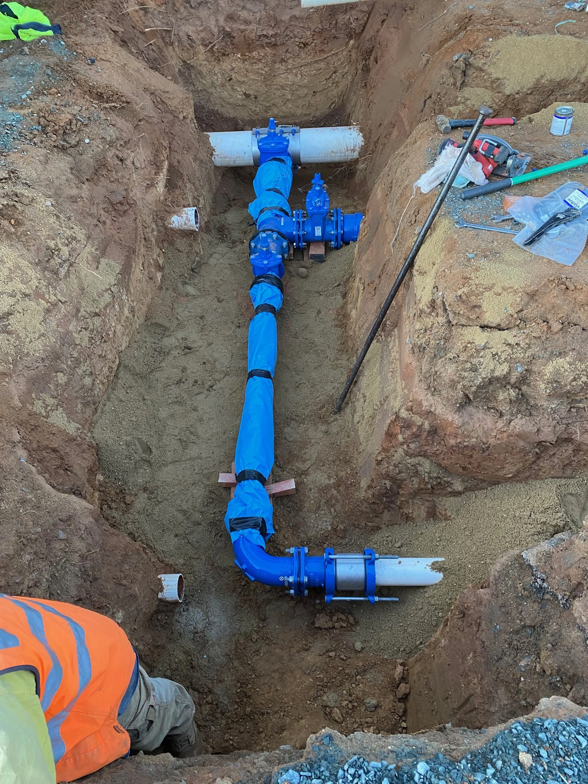 Installation of water pipes with blue valves and fittings in a trench, with construction tools and materials nearby.