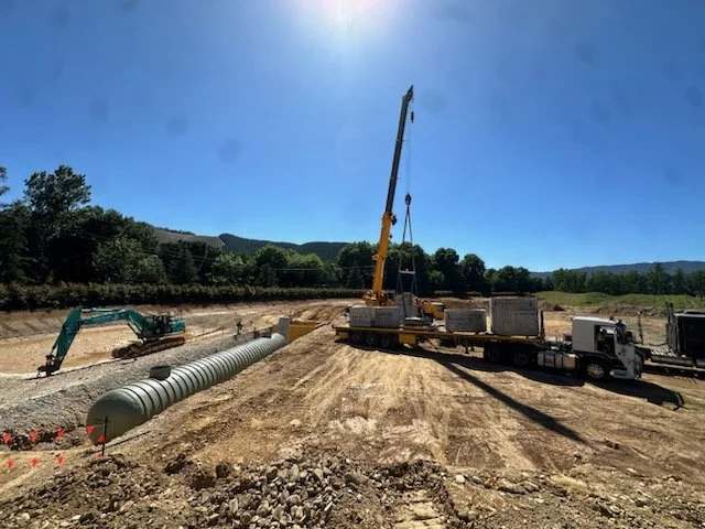 Construction site with a crane lifting equipment, a truck, and a large pipe on the ground