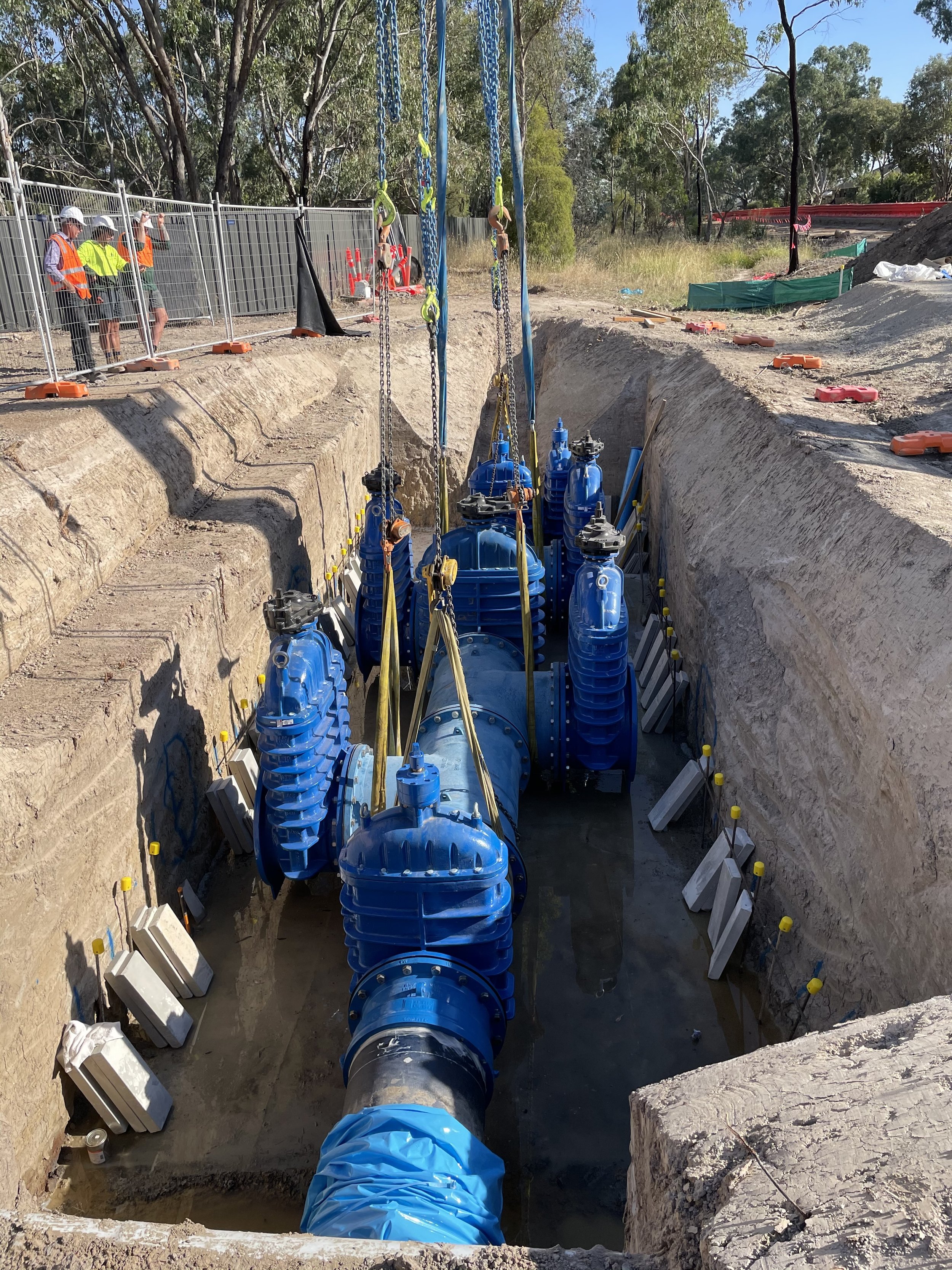 Construction workers inspecting a large pipeline installation in a deep trench, with blue fittings