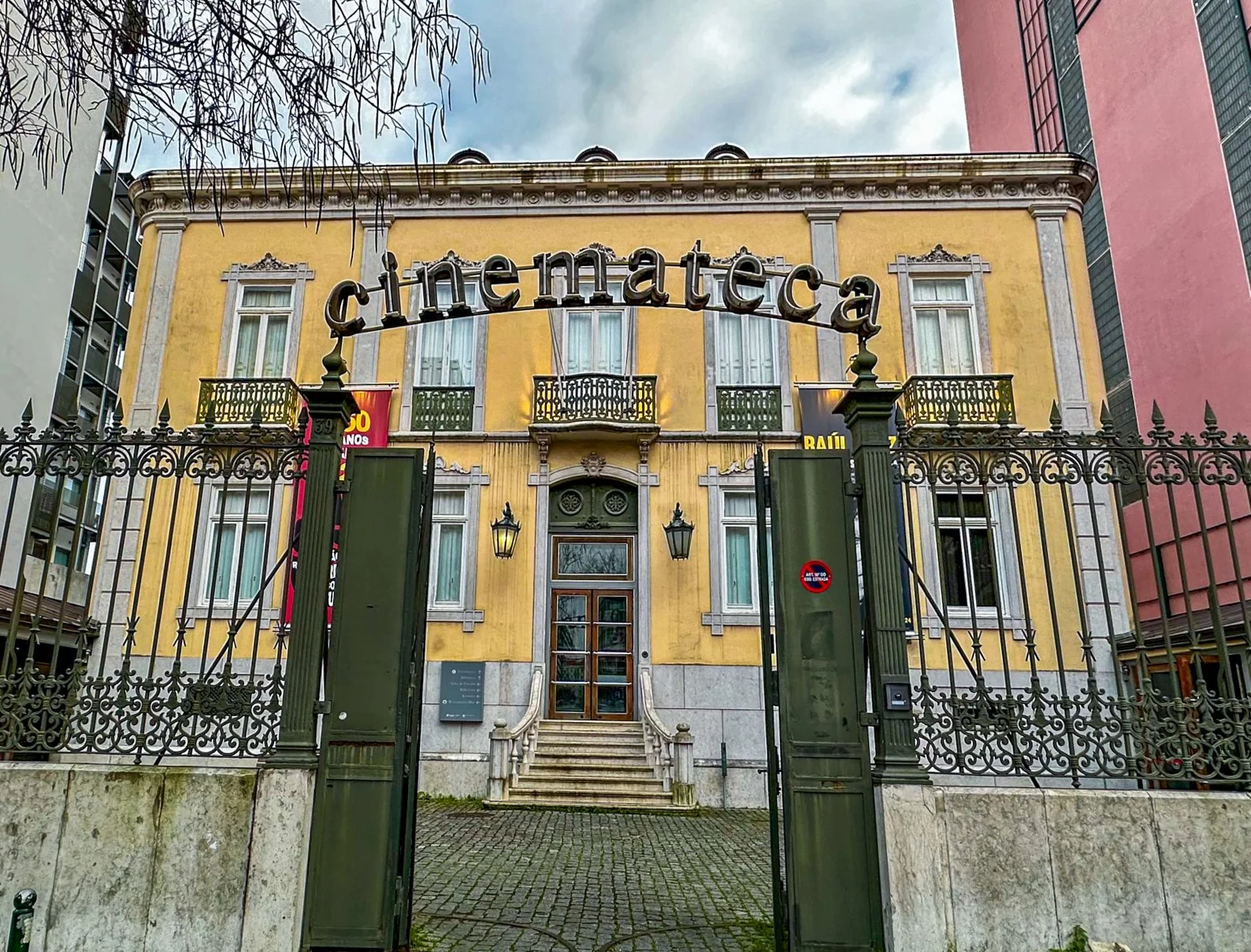 Entrada da cinemateca com portão de grades e em cima as letras cinemateca, edifício amarelo.