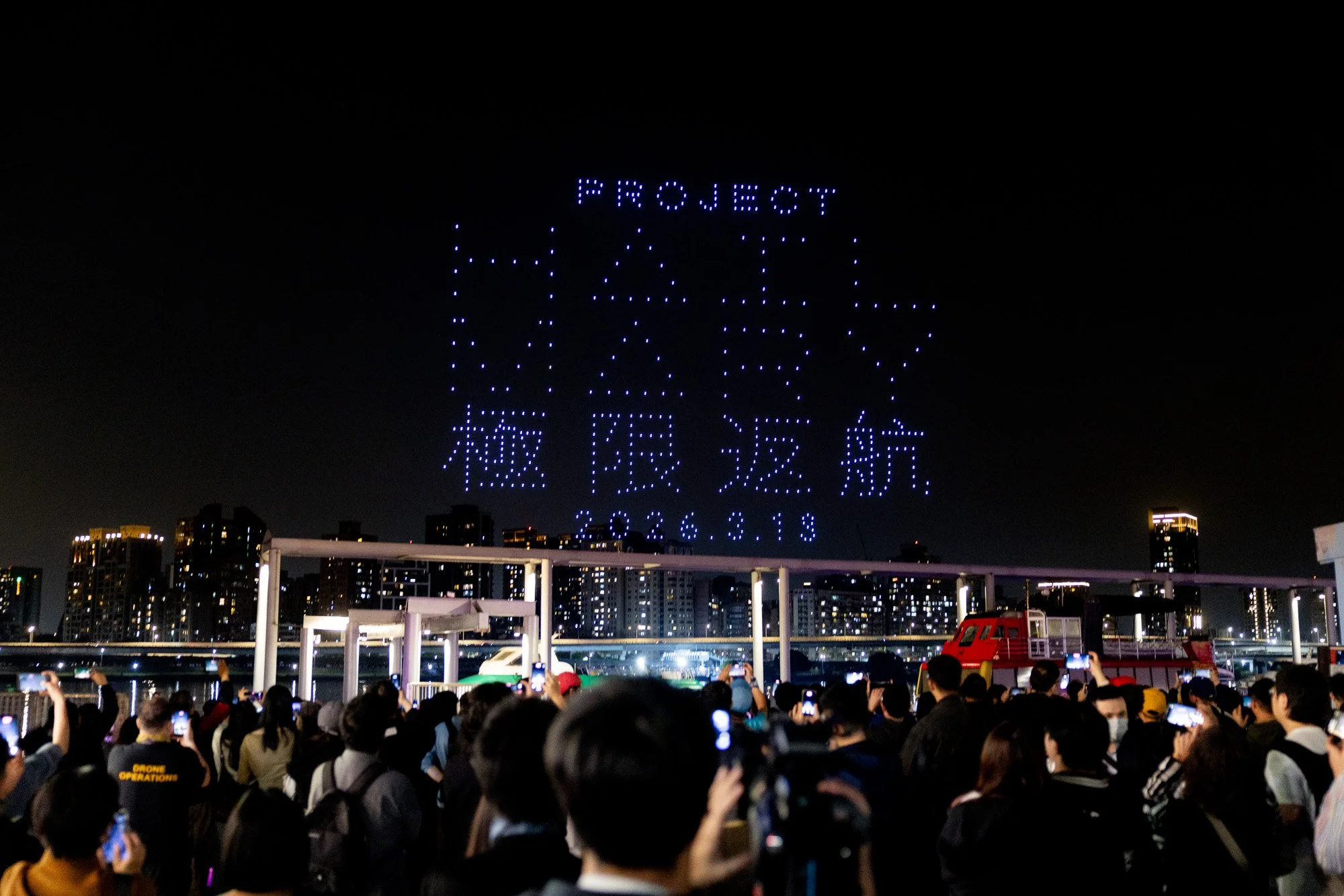 Crowd watching a drone light show above the Taipei skyline during a launch activation.