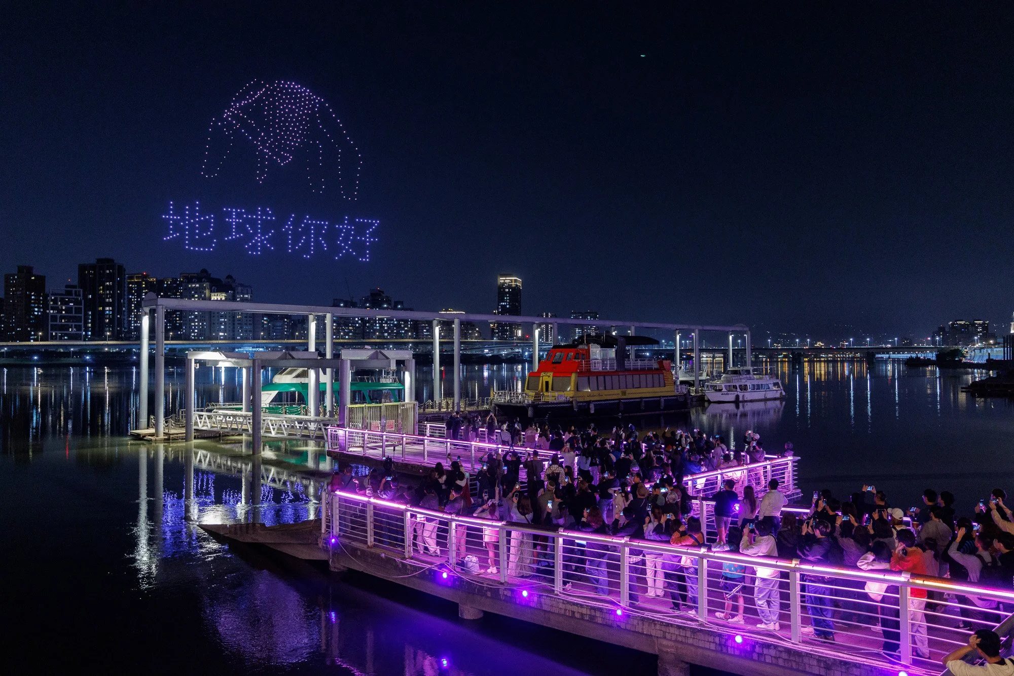 Waterfront activation with illuminated boats and drone visuals over Taipei at night.