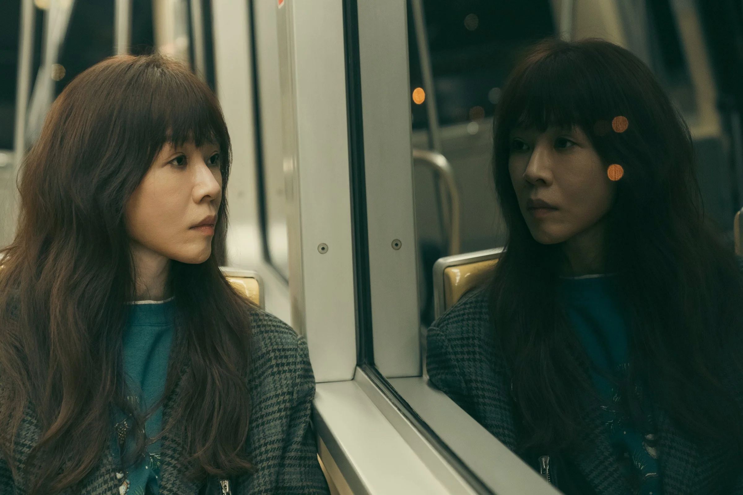 Narrative unit still from Forget You Not featuring a female character reflected in a train window, capturing a quiet moment of introspection and emotional distance.
