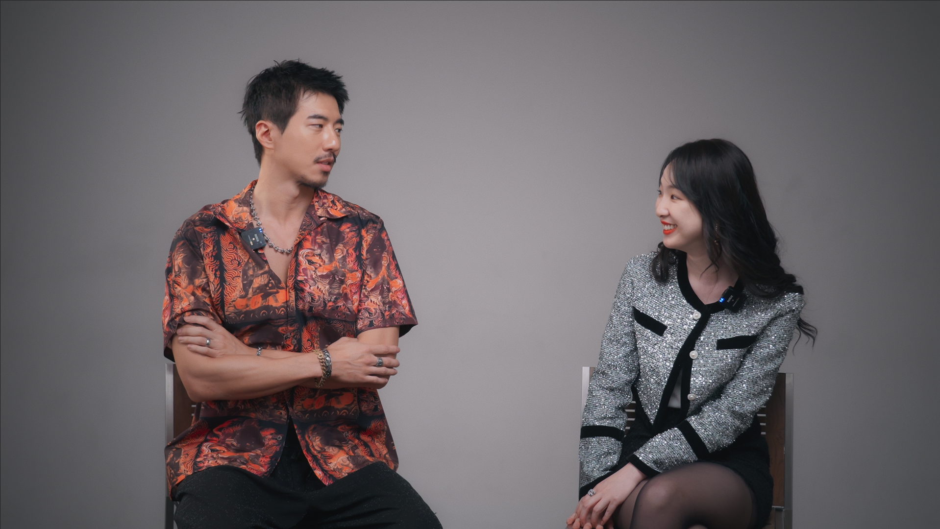 EPK interview still showing two lead talents in conversation against a neutral studio background.