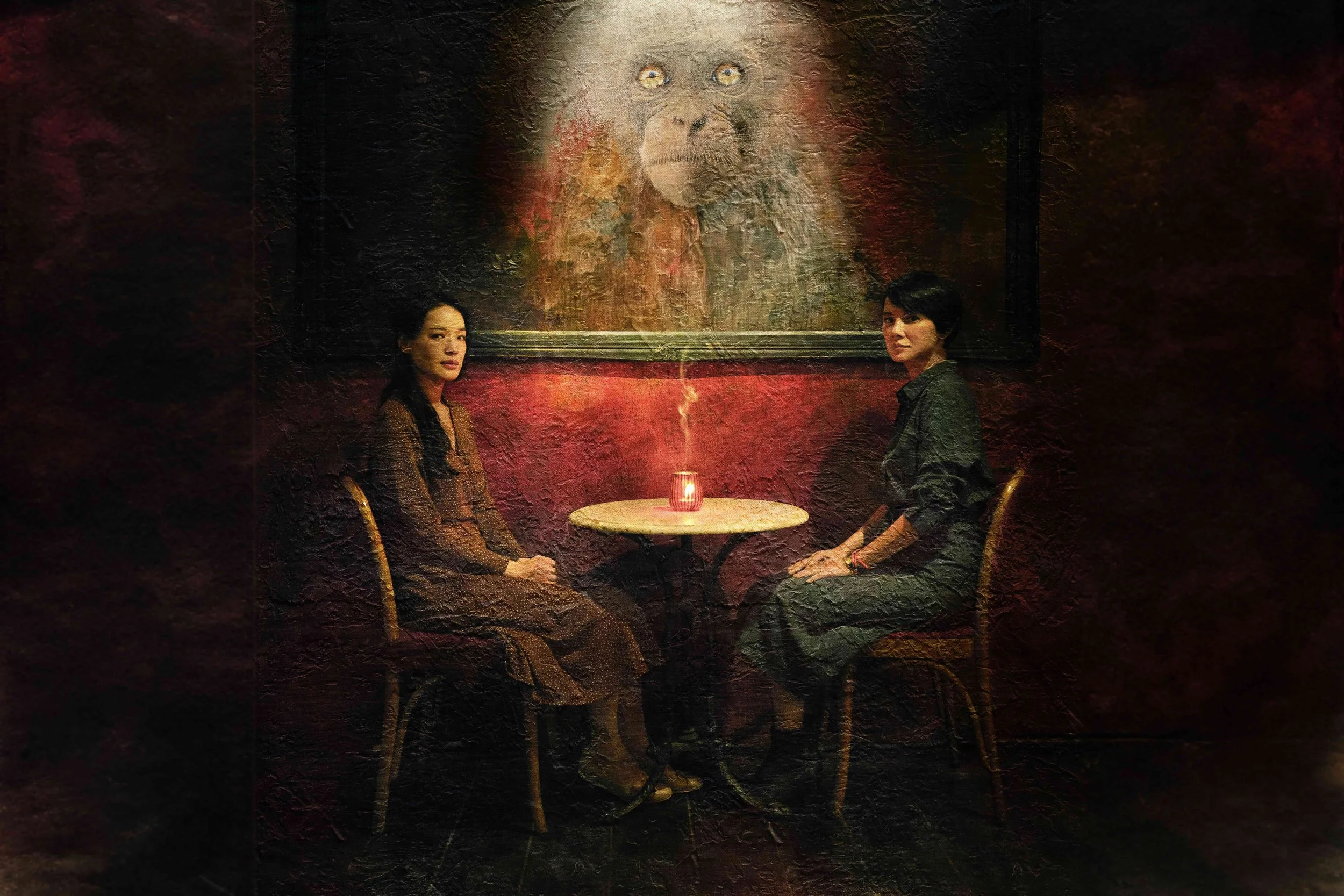 Key campaign image from The Resurrected, depicting two women seated in a dimly lit café beneath a haunting primate painting.