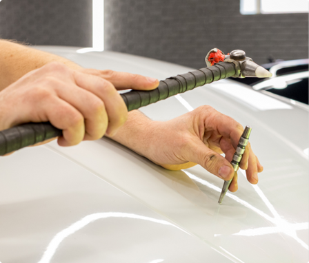 A person using a precise tool to draw a white line on the surface of a white car.