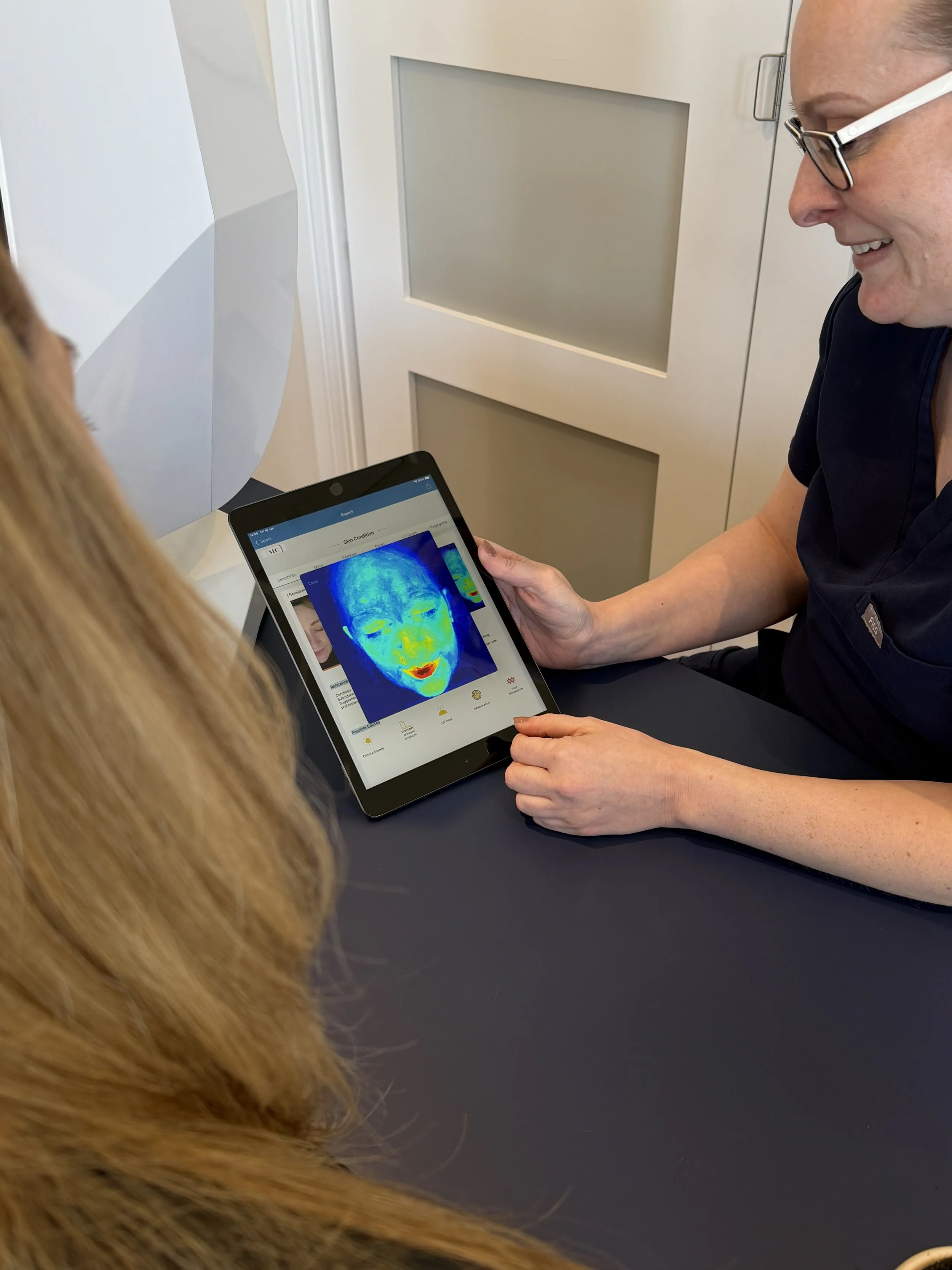 A healthcare professional showing a thermal imaging scan of a woman's face on a tablet screen to a patient.