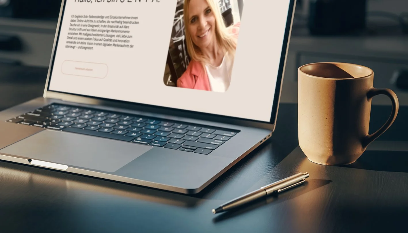 MacBook-Laptop auf einem Tisch mit einer Webseite, die ein Foto einer Frau zeigt, eine Tasse, einen Kugelschreiber und eine Sonnenlichtreflexion auf der Oberfläche.
