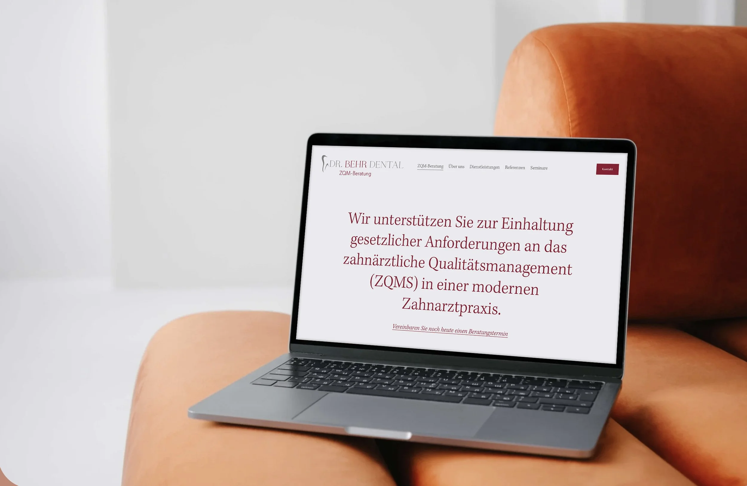 Ein Laptop auf einem orangefarbenen Sitzsack mit einer Webseite auf dem Bildschirm, die die Zahnarztpraxis Dr. Behr zeigt.