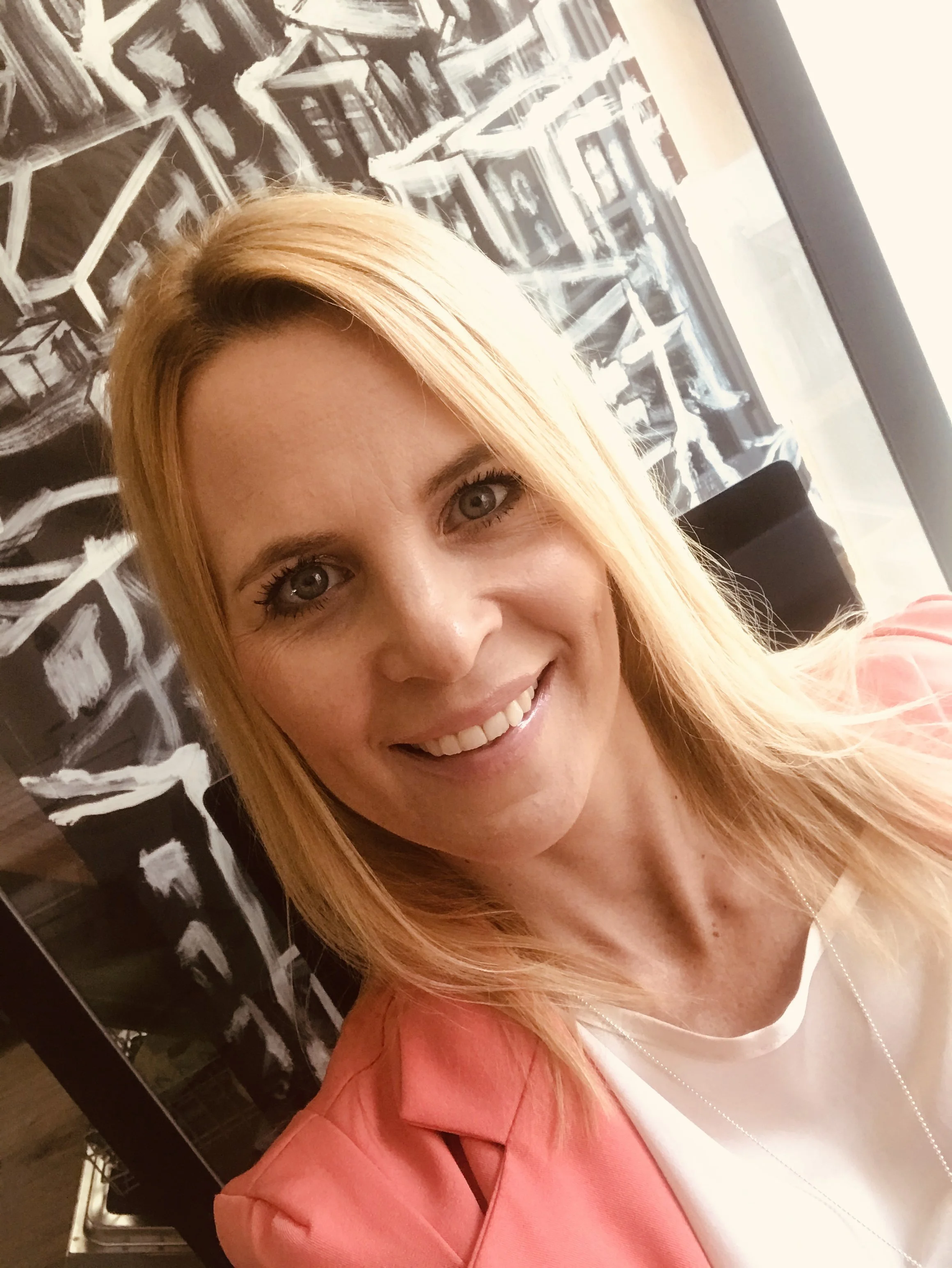 Ein Porträt einer lächelnden Frau mit blonden Haaren vor einer schwarzen und weißen Kunstinstallation.