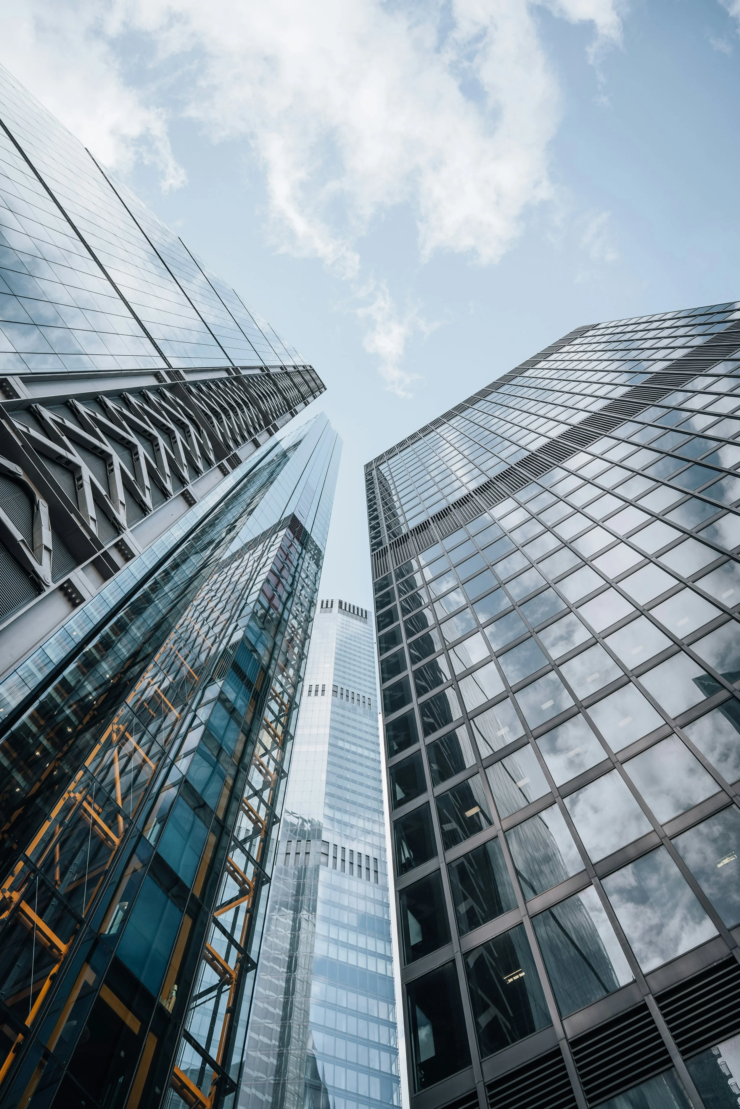 Low-angle view of tall modern glass skyscrapers reflecting clouds and sky.