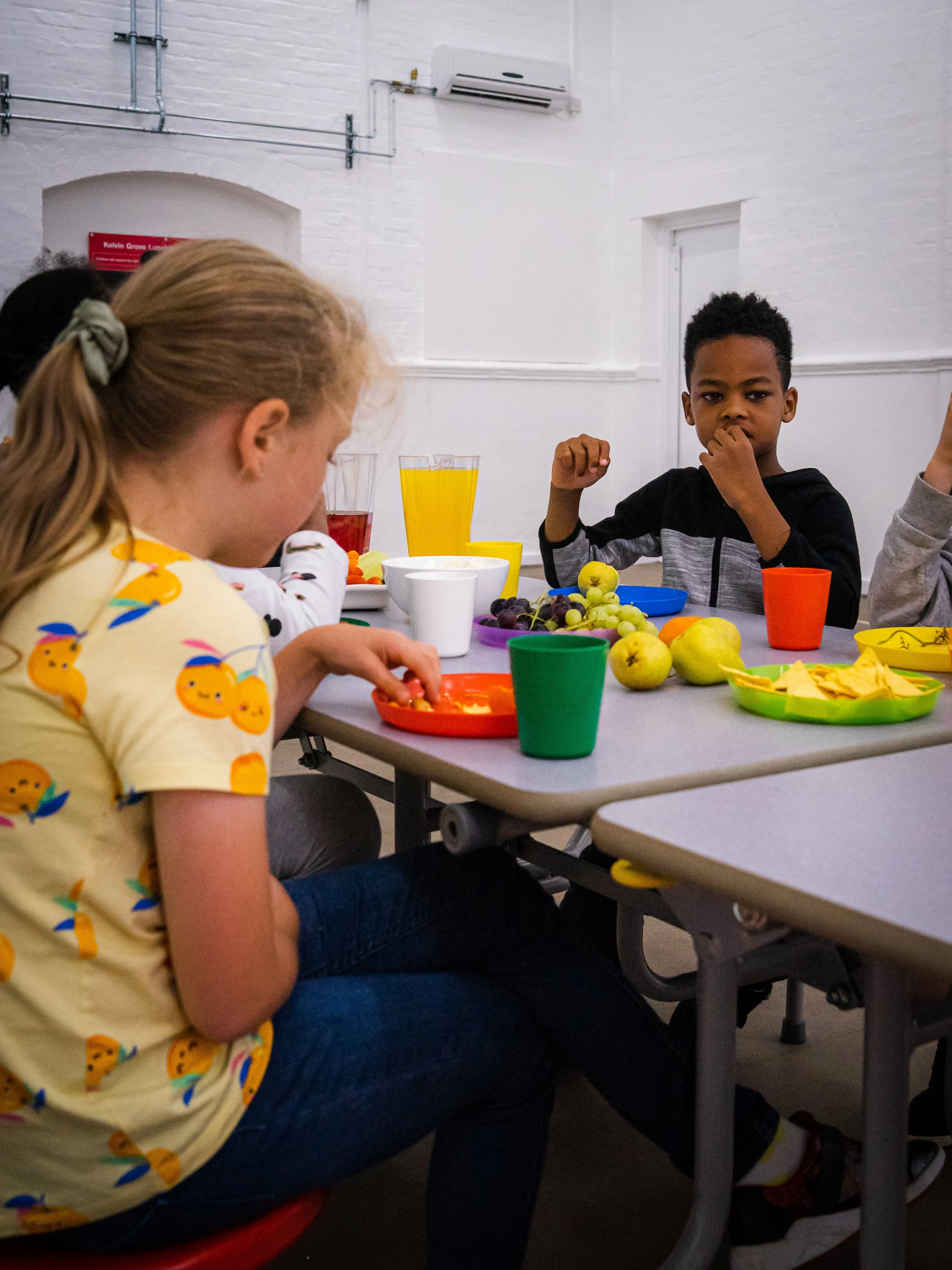 Children sitting at a table with fruit, snacks, and drinks, enjoying a snack at Global Camps holiday camp