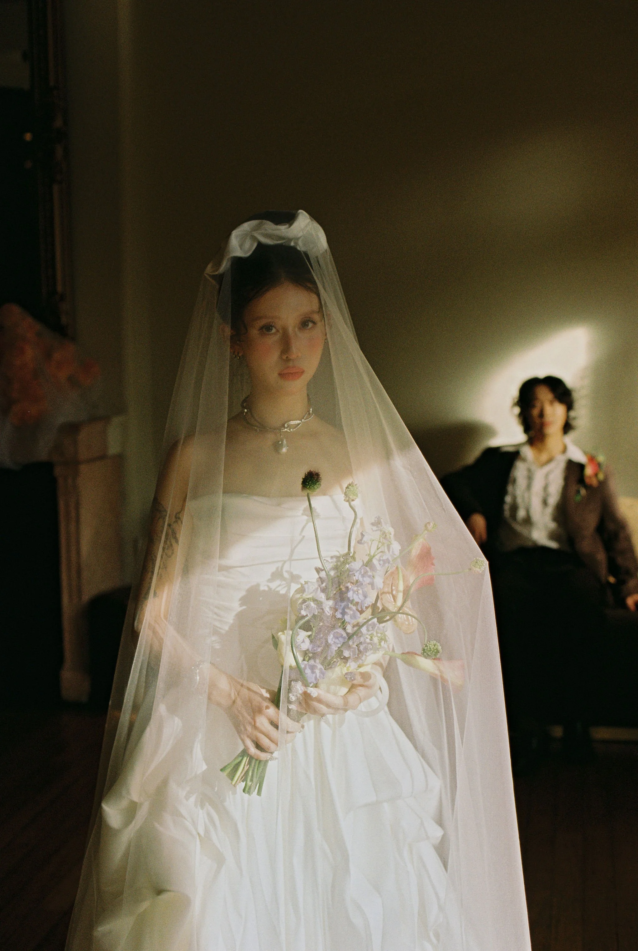 A woman dressed as a bride holding a bouquet of flowers, with another woman in the background.