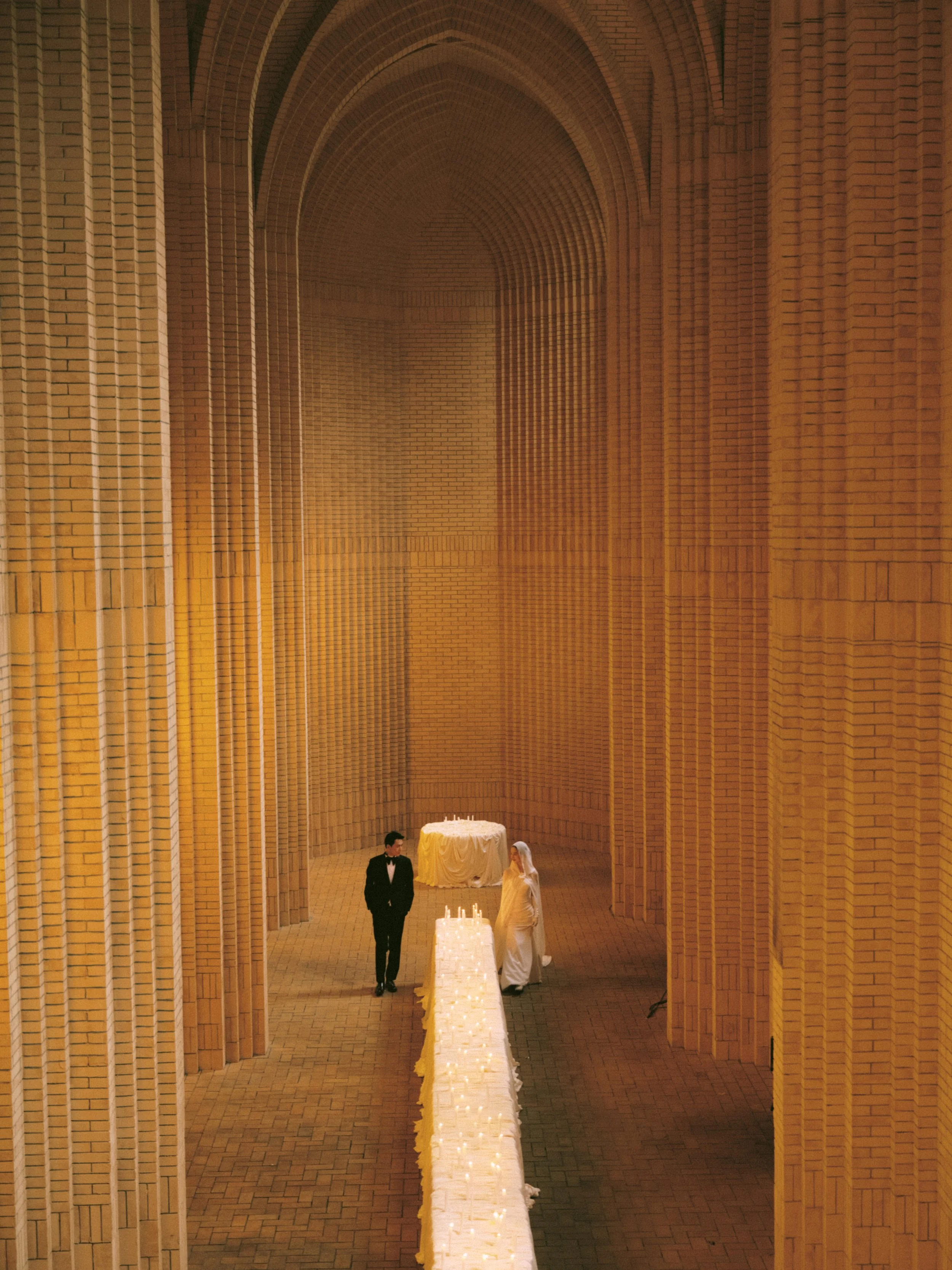 A bride and groom standing under a large brick archway, with wedding candles and table decor.