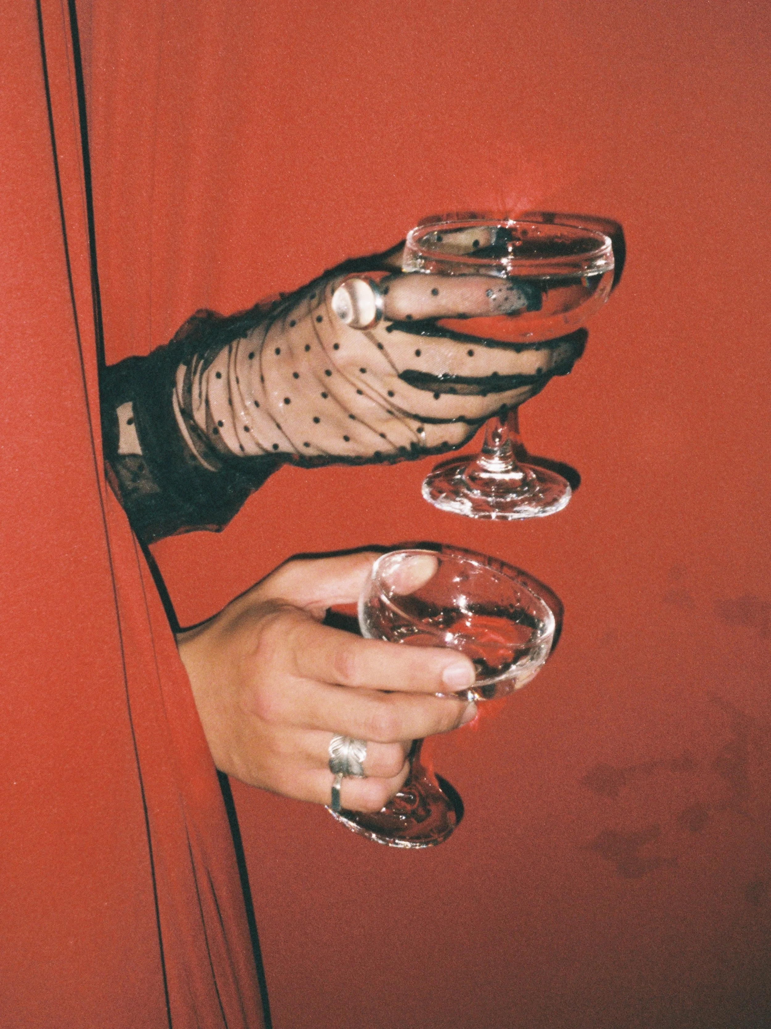 A person's hand holding a glass of red wine, with a red background.