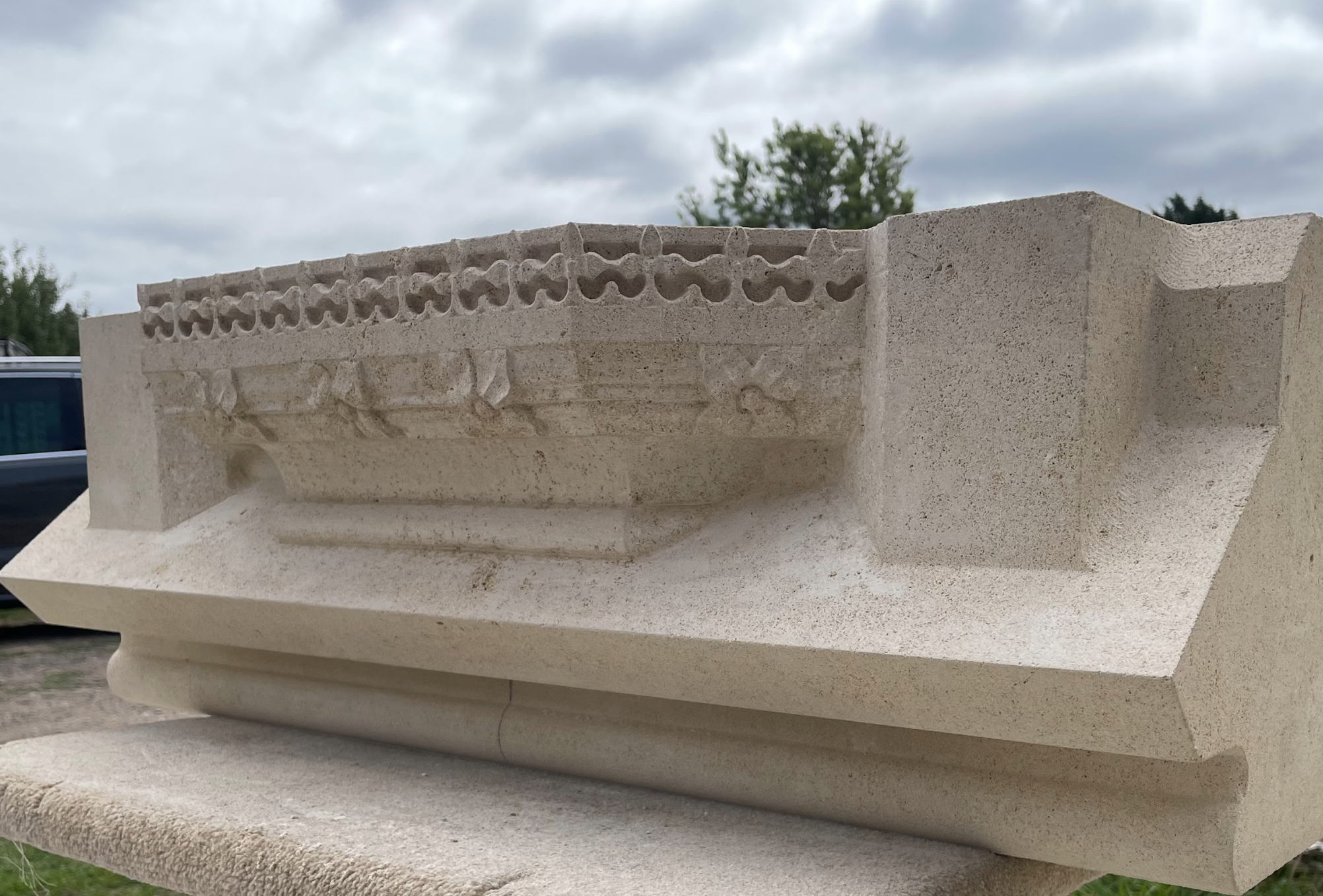 A carved stone relief with intricate patterns and figures, likely of historical or archaeological significance, displayed outdoors against a cloudy sky.
