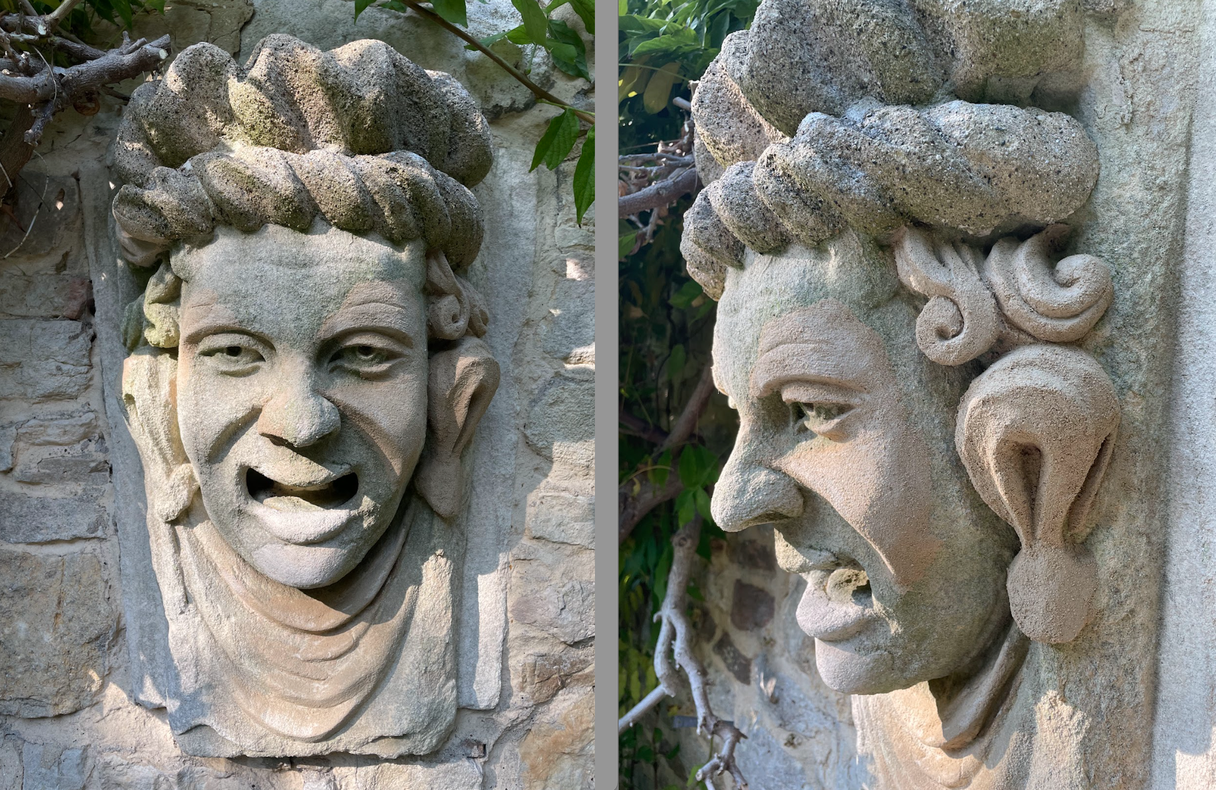 Two stone wall sculptures of expressive faces, one smiling and the other appearing angry or shouting, set against a stone wall with greenery around.