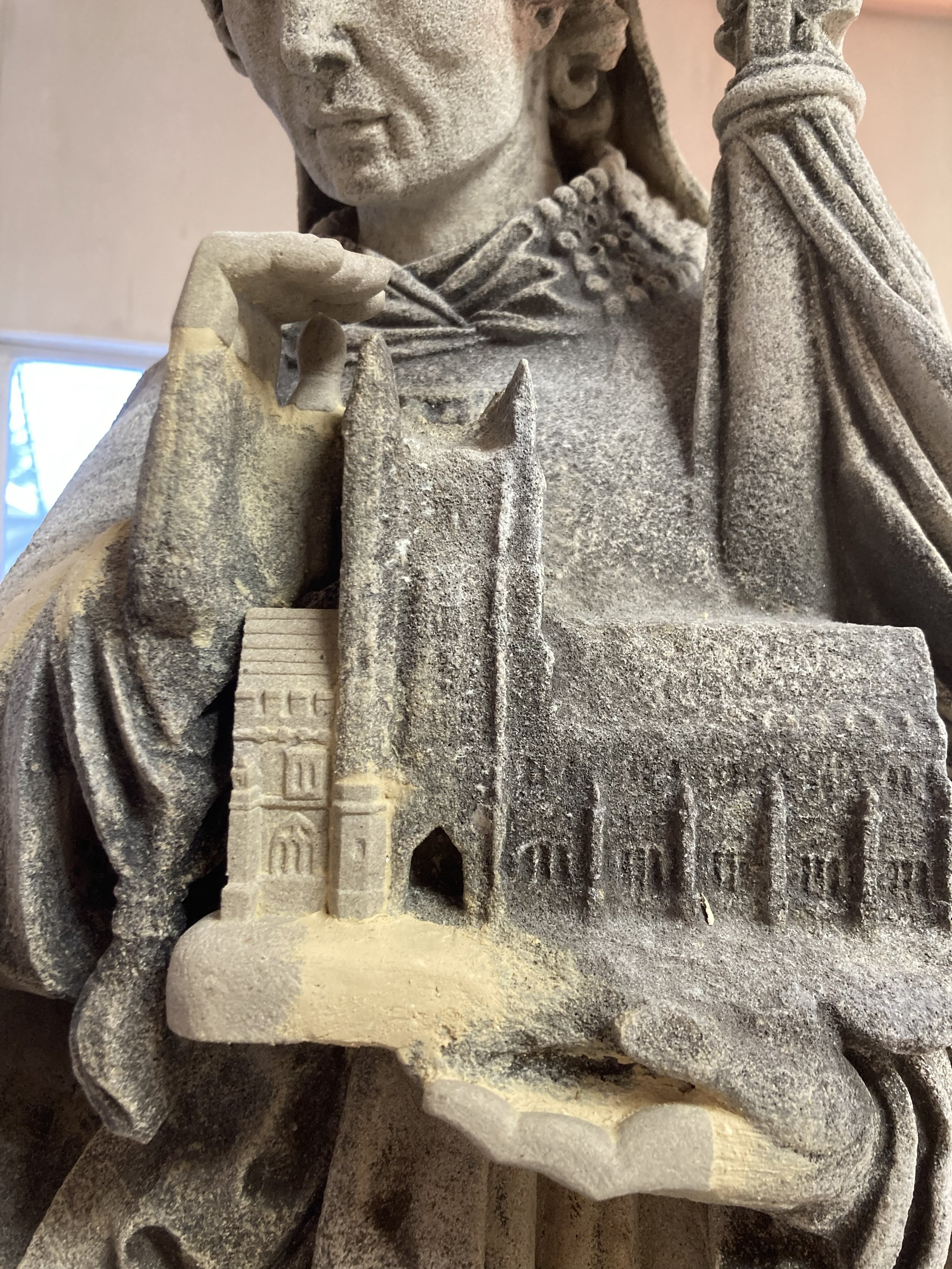 Close-up of a stone sculpture depicting a person holding a book, with detailed carvings of buildings or architectural elements on the book.