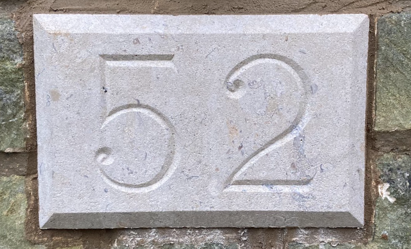 A rectangular stone plaque with the numbers '32' engraved in large font, mounted on a brick wall.
