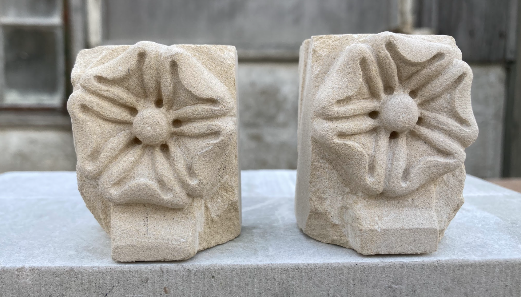Two carved stone blocks with floral designs, placed on a flat surface outdoors.