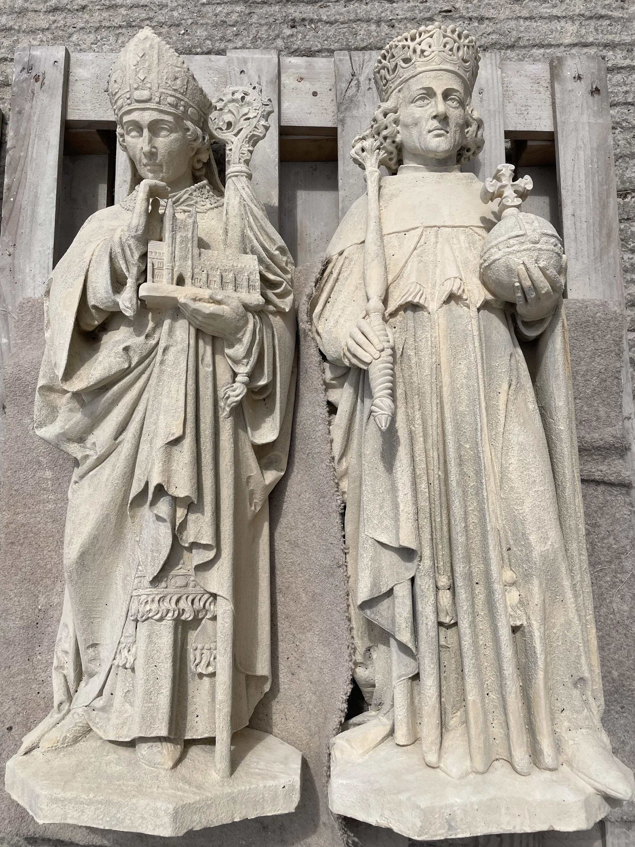 Stone sculptures of two regal women, each wearing crowns and holding symbolic items. The woman on the left holds a model of a building and a staff, while the woman on the right holds a scepter and an orb.